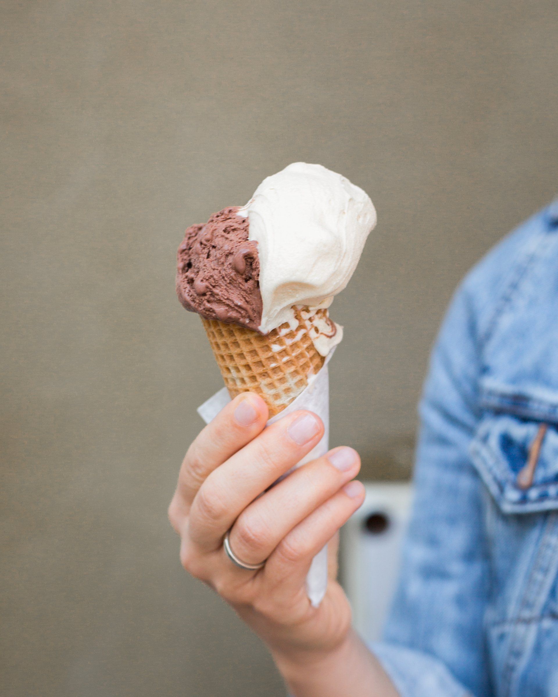 Hand holding a waffle cone with chocolate & vanilla ice cream against a blurred background. Grasshopper Farms Knightdale, NC