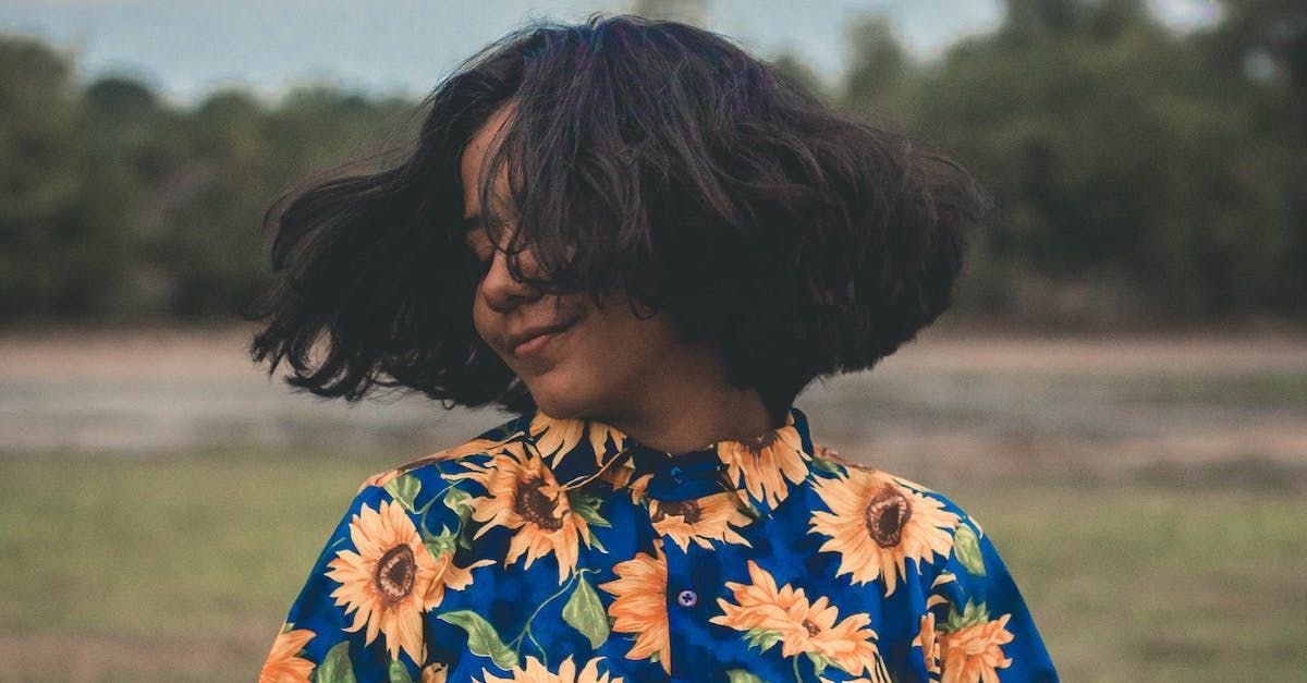 A woman wearing a blue shirt with sunflowers on it is standing in a field.