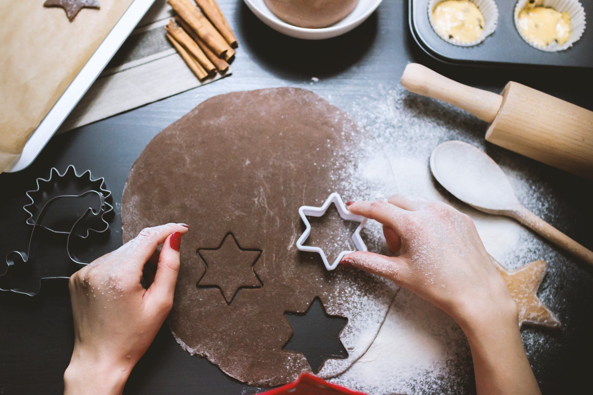Hands cutting star-shaped cookies from dough on a floured surface, with baking tools and ingredients.