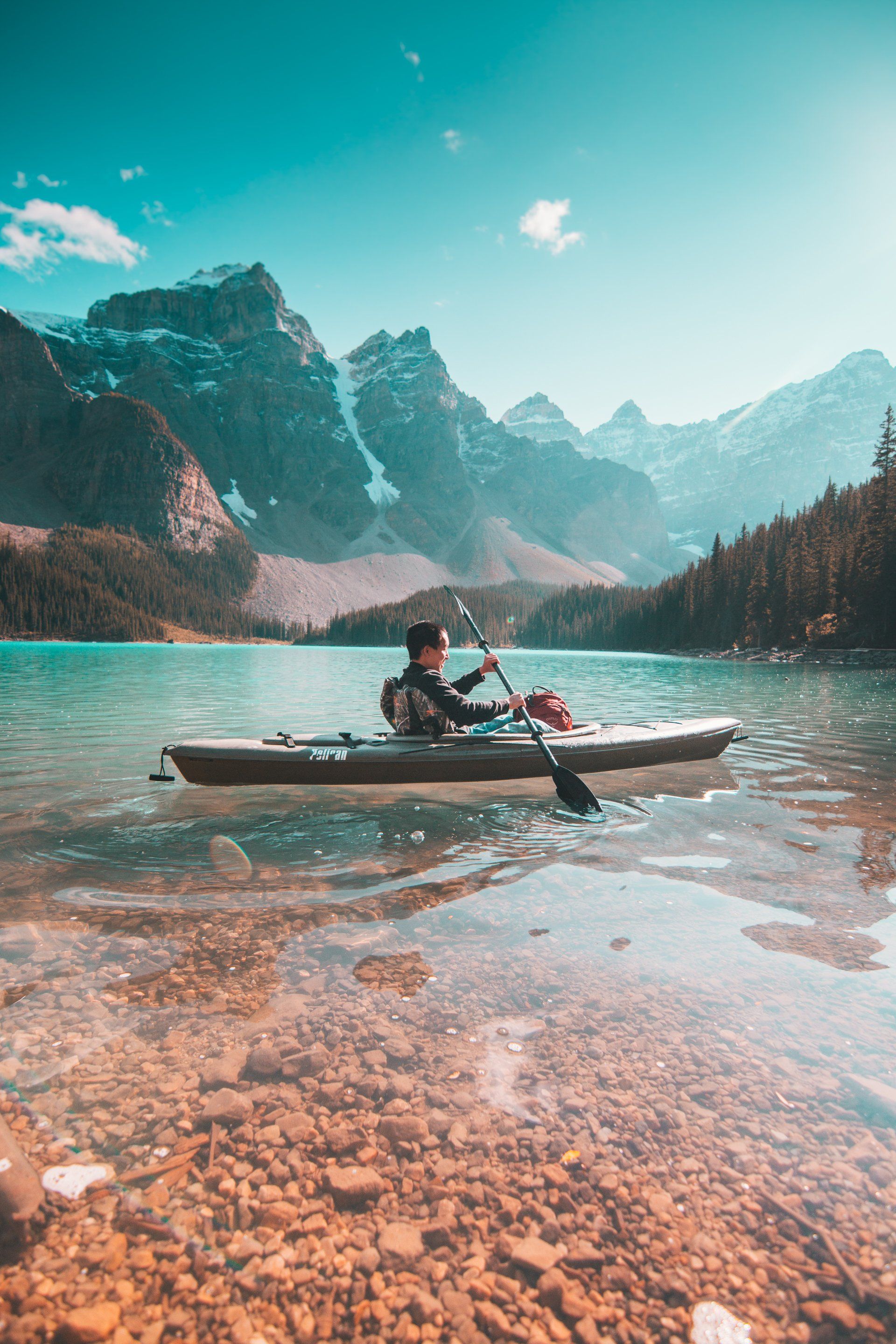 A person is rowing a kayak on a lake with mountains in the background.