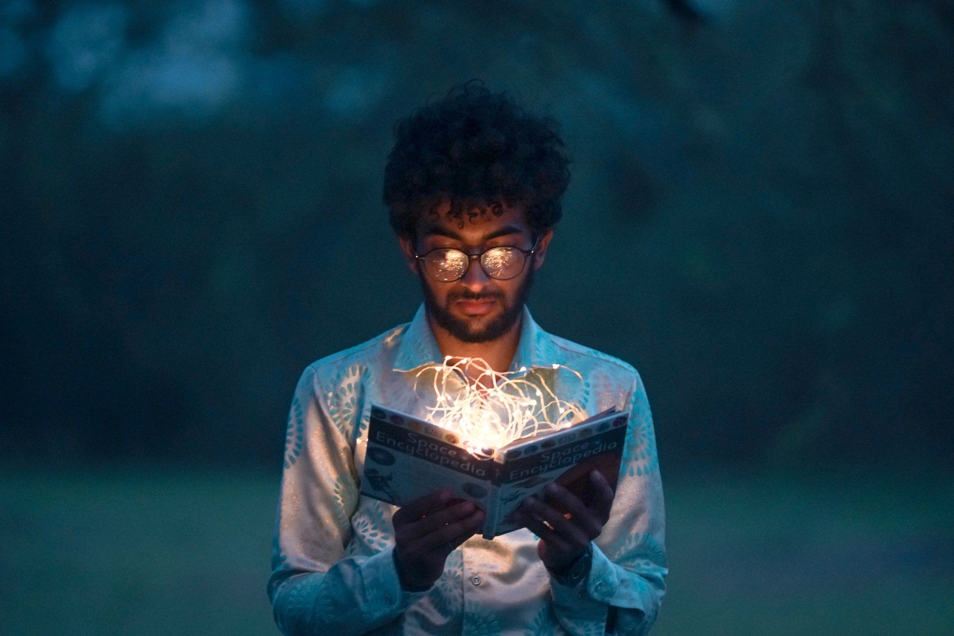 A man is reading a book with lights coming out of it.