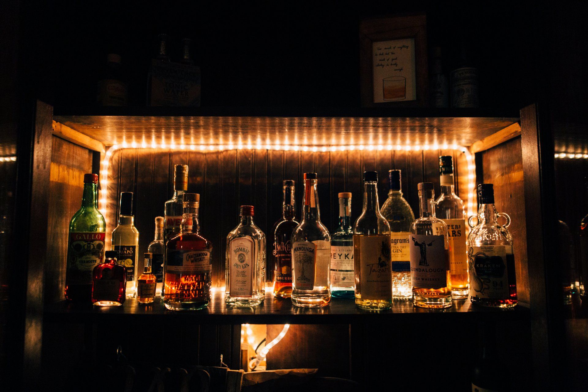Bottles of alcohol backlit on a bar shelf.