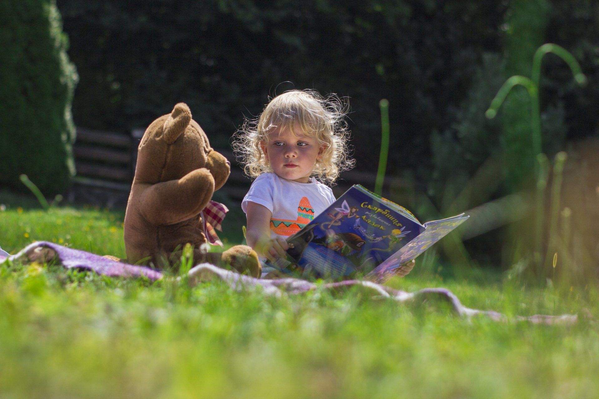 Toddler holding a book sitting next to a teddy bear
