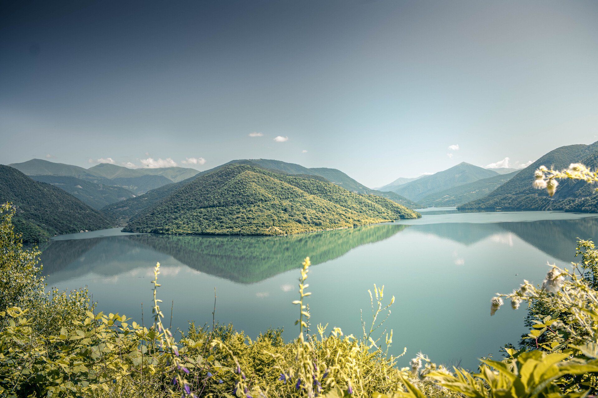 A lake surrounded by mountains and trees on a sunny day
