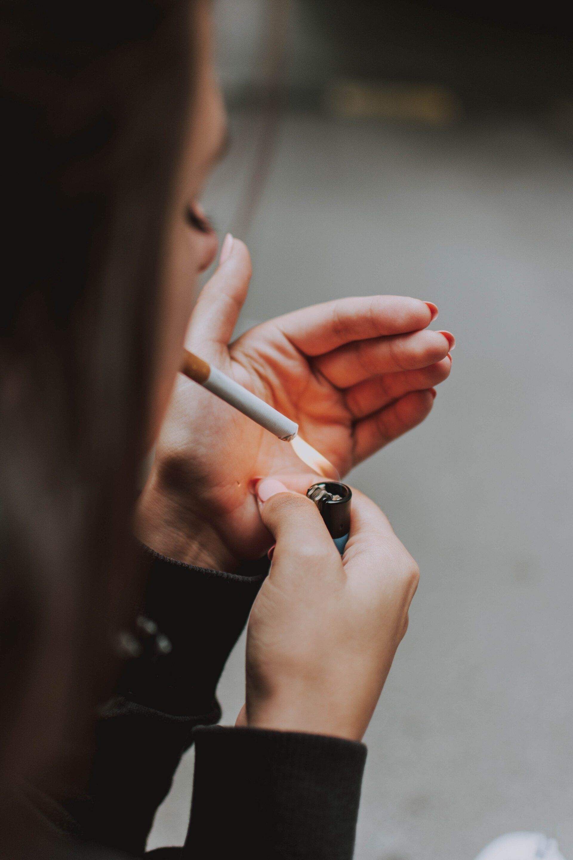 Person lighting a cigarette with a lighter, seen from over the shoulder.