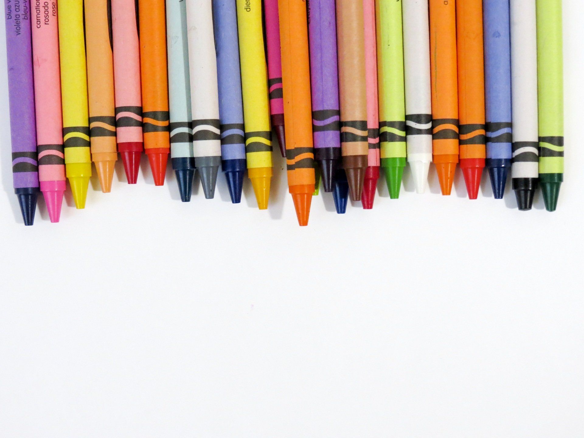 Row of various colored crayons on a white background.
