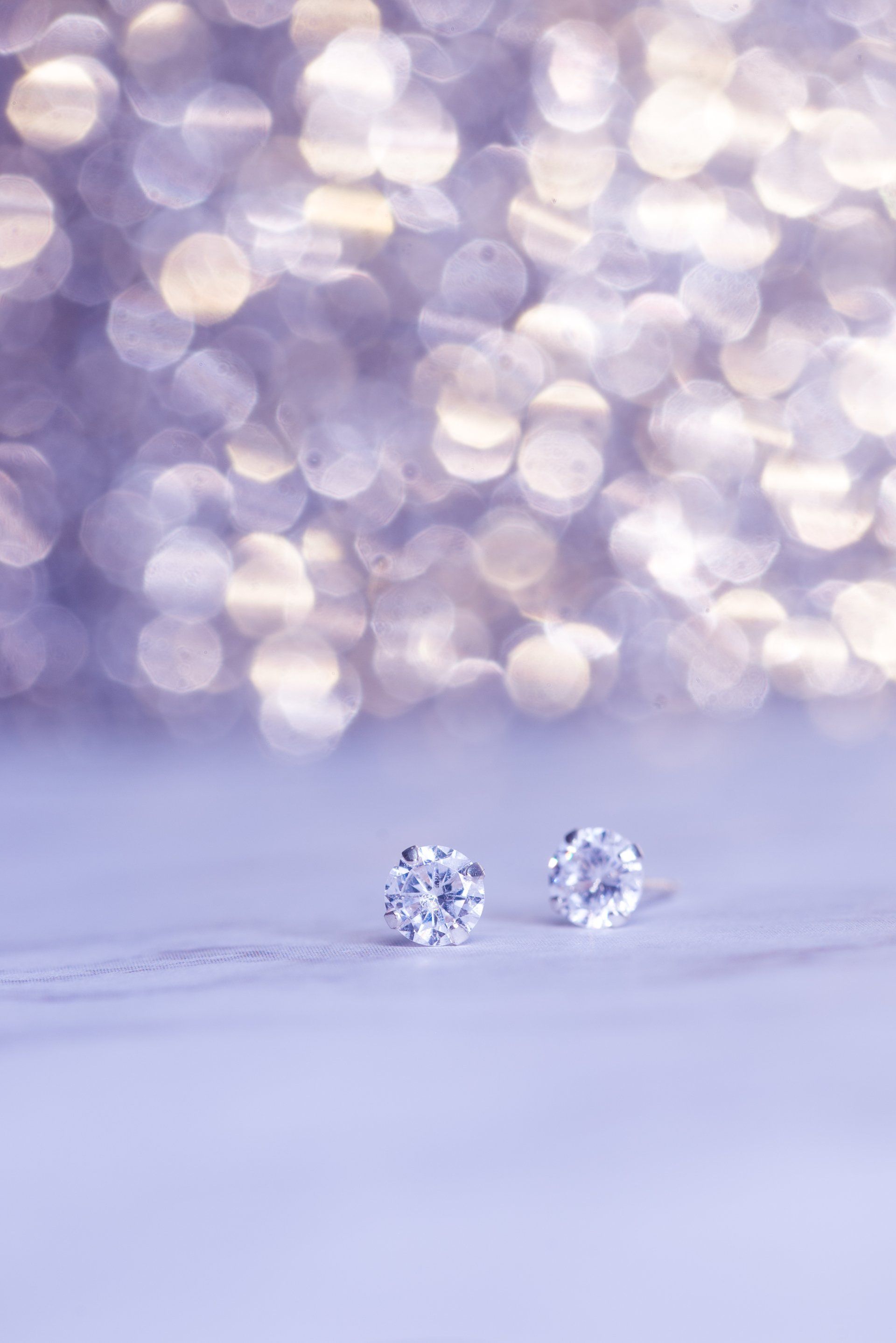 A pair of diamond stud earrings on a purple background.
