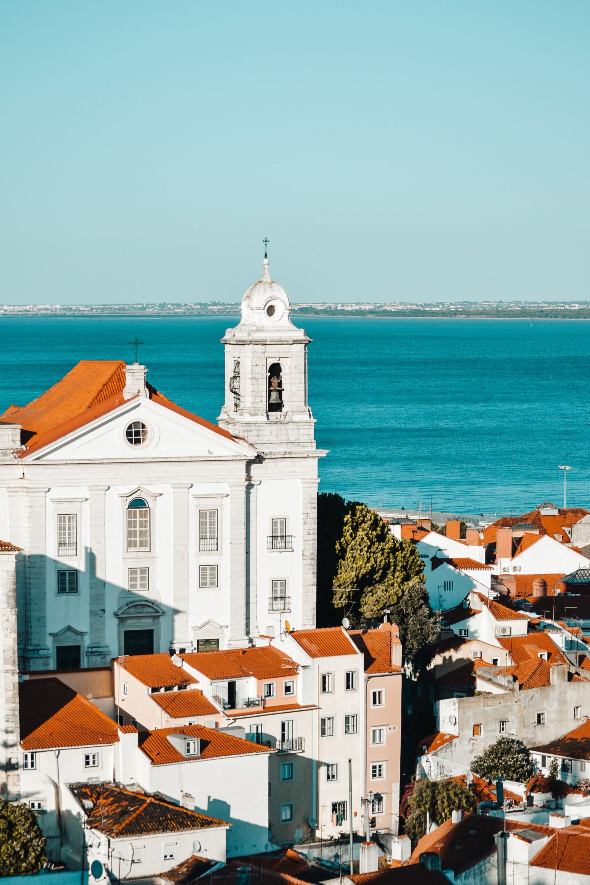 An aerial view of a city with a church and a bell tower overlooking the ocean.