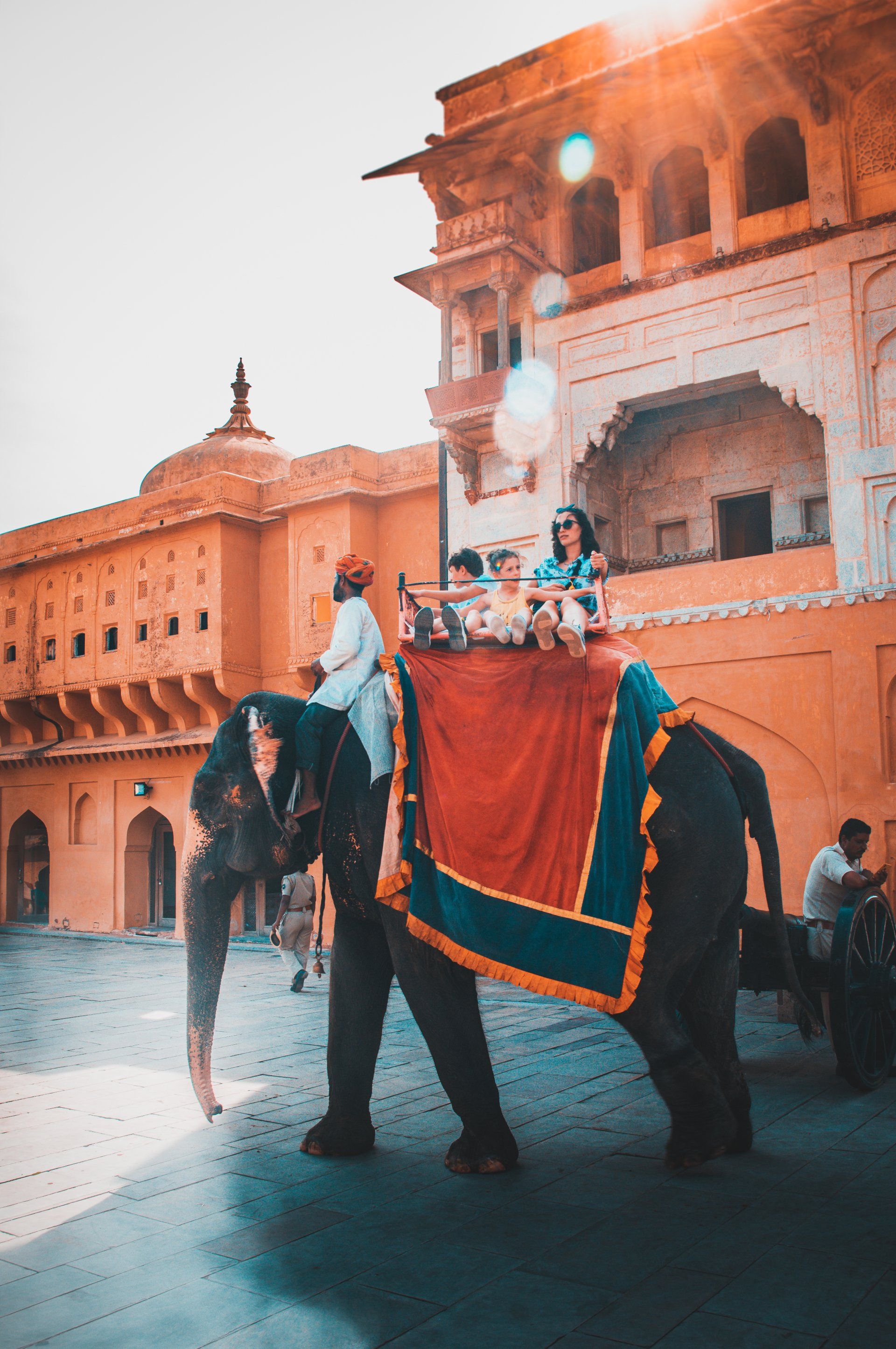 Elephant carrying tourists in front of an orange palace. Bright sunlight. jaipur