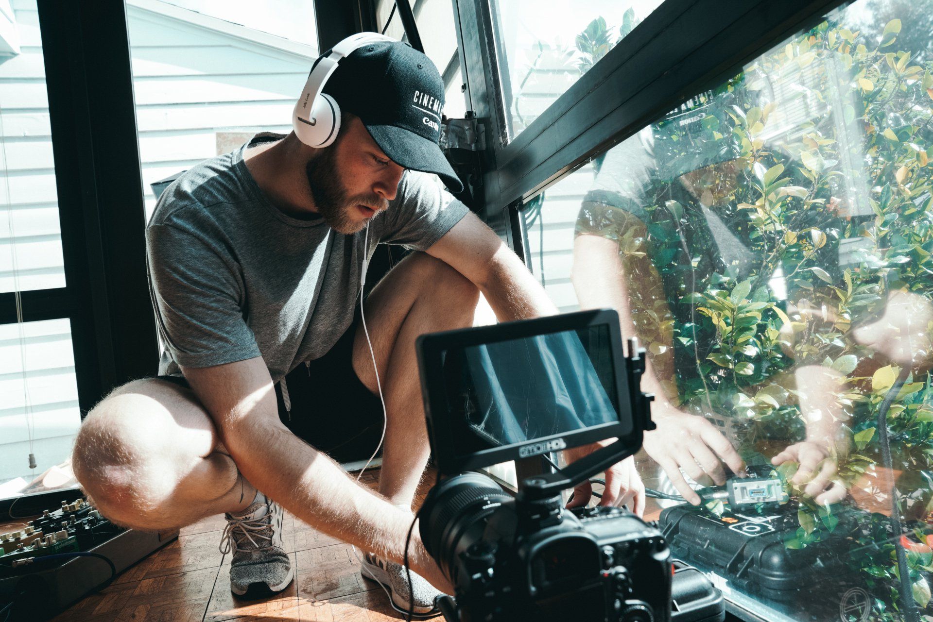 A man wearing headphones is kneeling down in front of a camera.