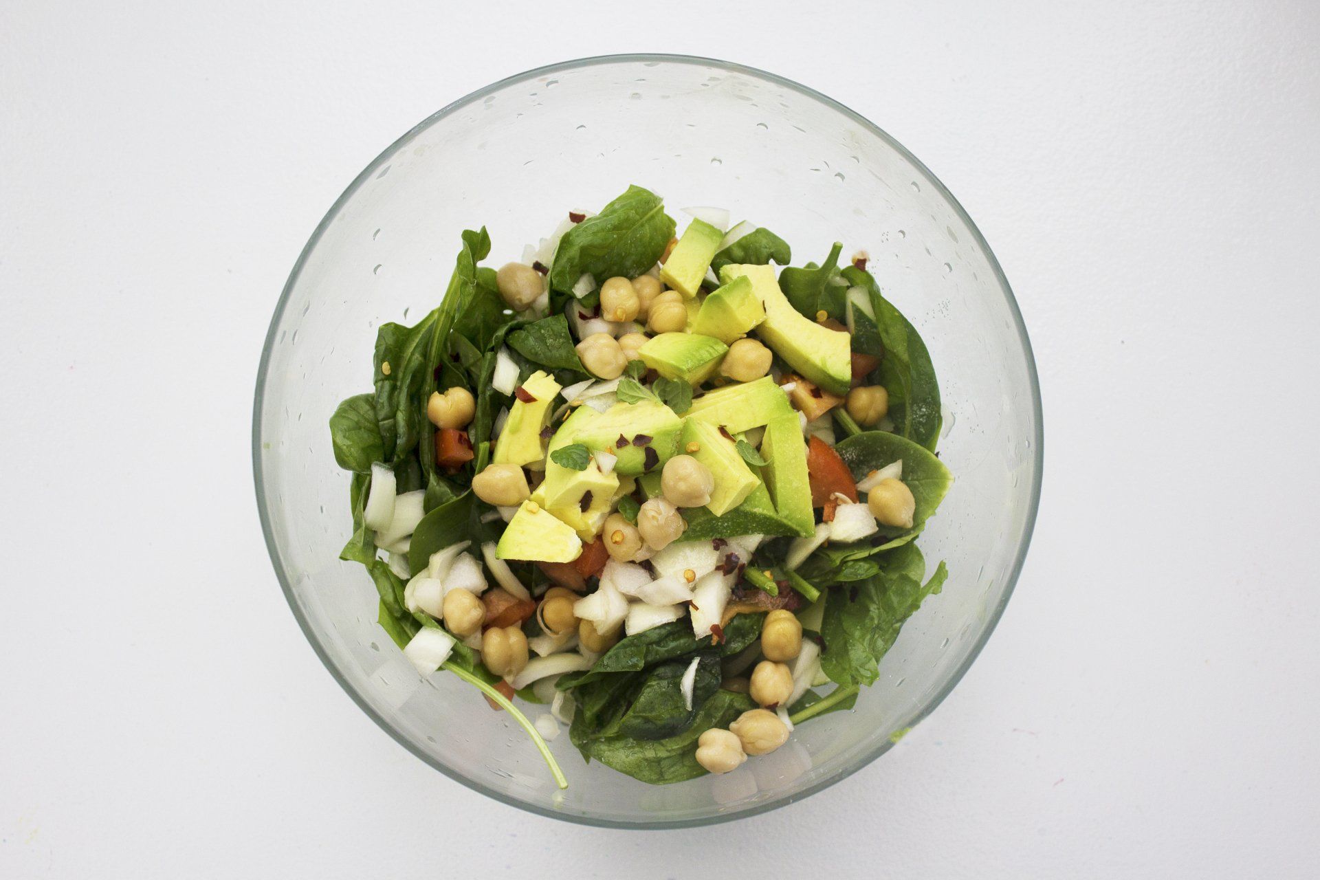 Salad in a clear bowl: spinach, chickpeas, avocado, onion.
