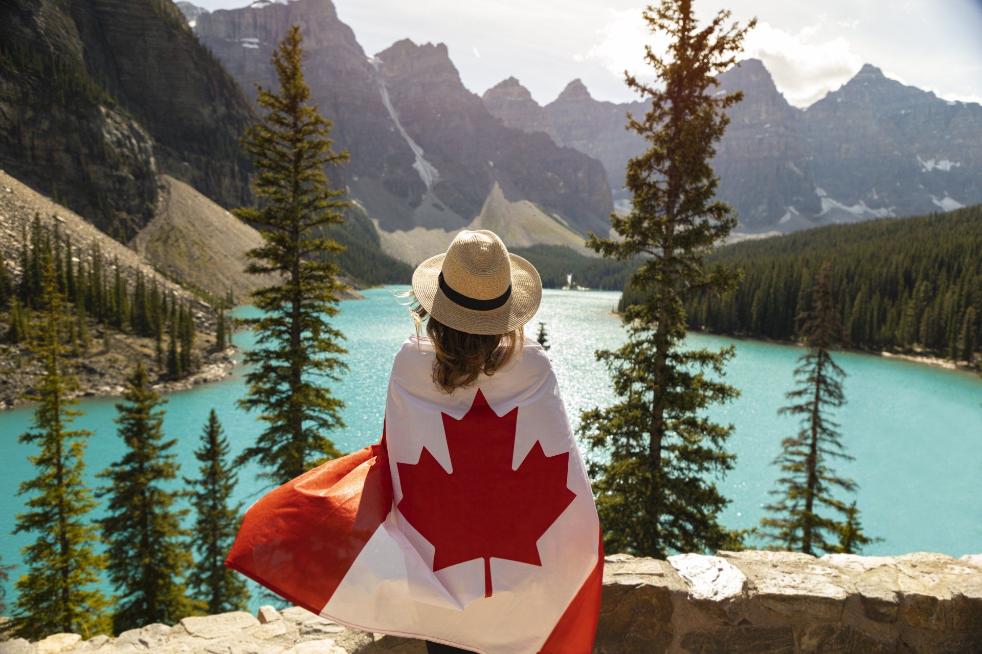A woman wrapped in a canadian flag is looking at a lake.