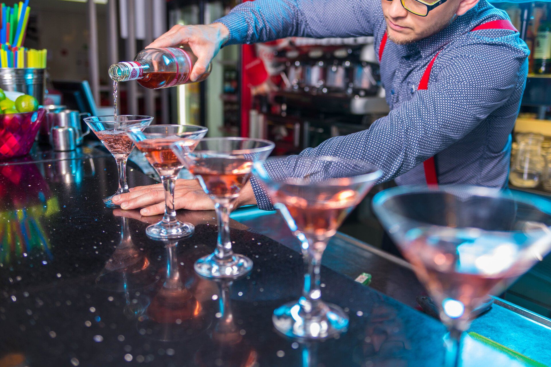 A bartender is pouring a drink into a martini glass at a bar.