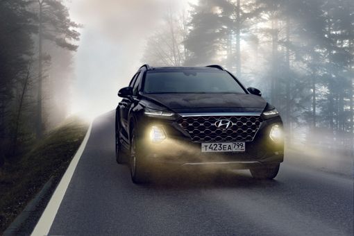 A black suv is driving down a foggy road.