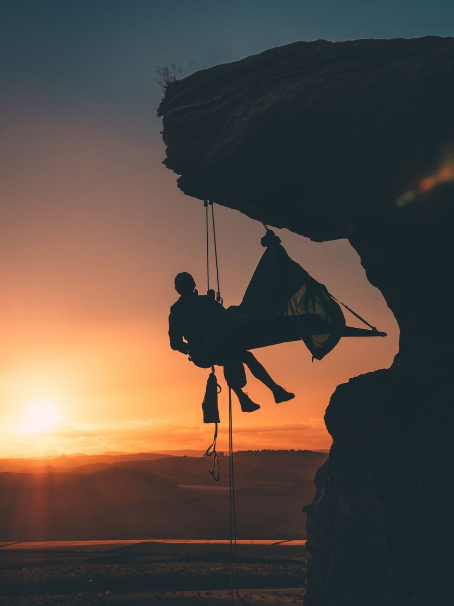 Eine Person sitzt bei Sonnenuntergang in einer Hängematte auf einer Klippe.