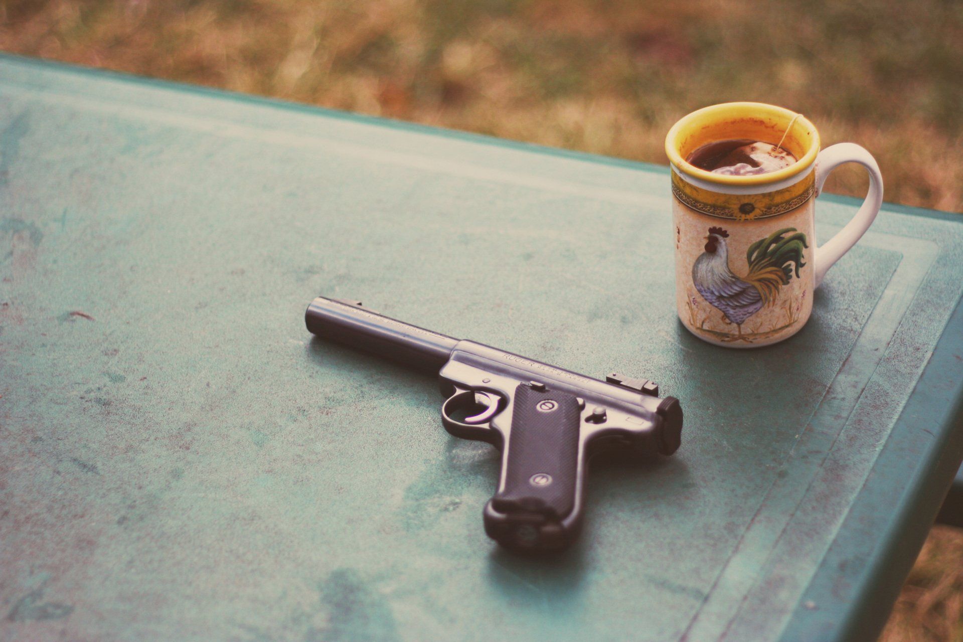 Handgun on a green table beside a patterned mug of coffee outdoors