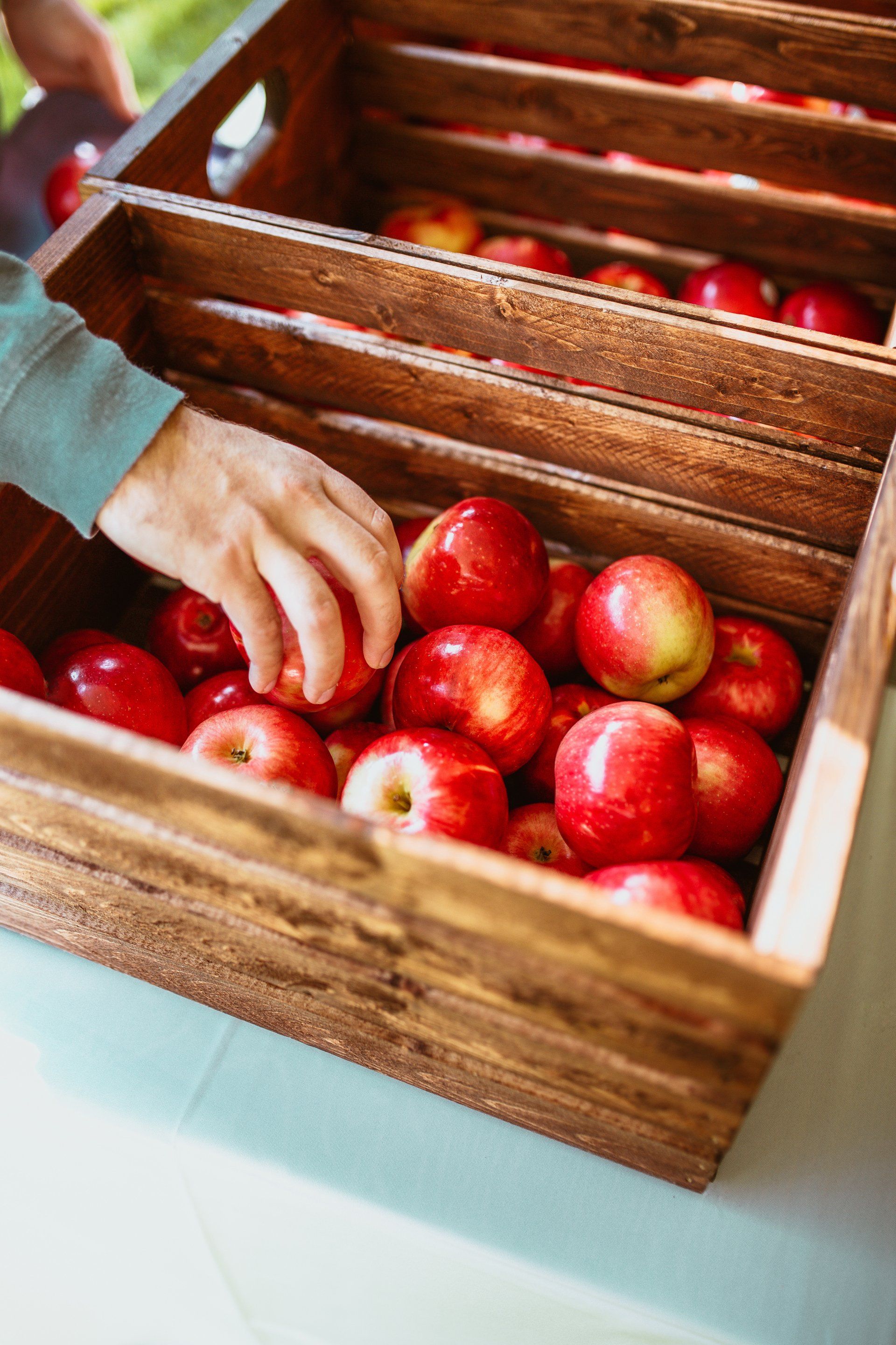 A person is picking apples out of a wooden crate.
