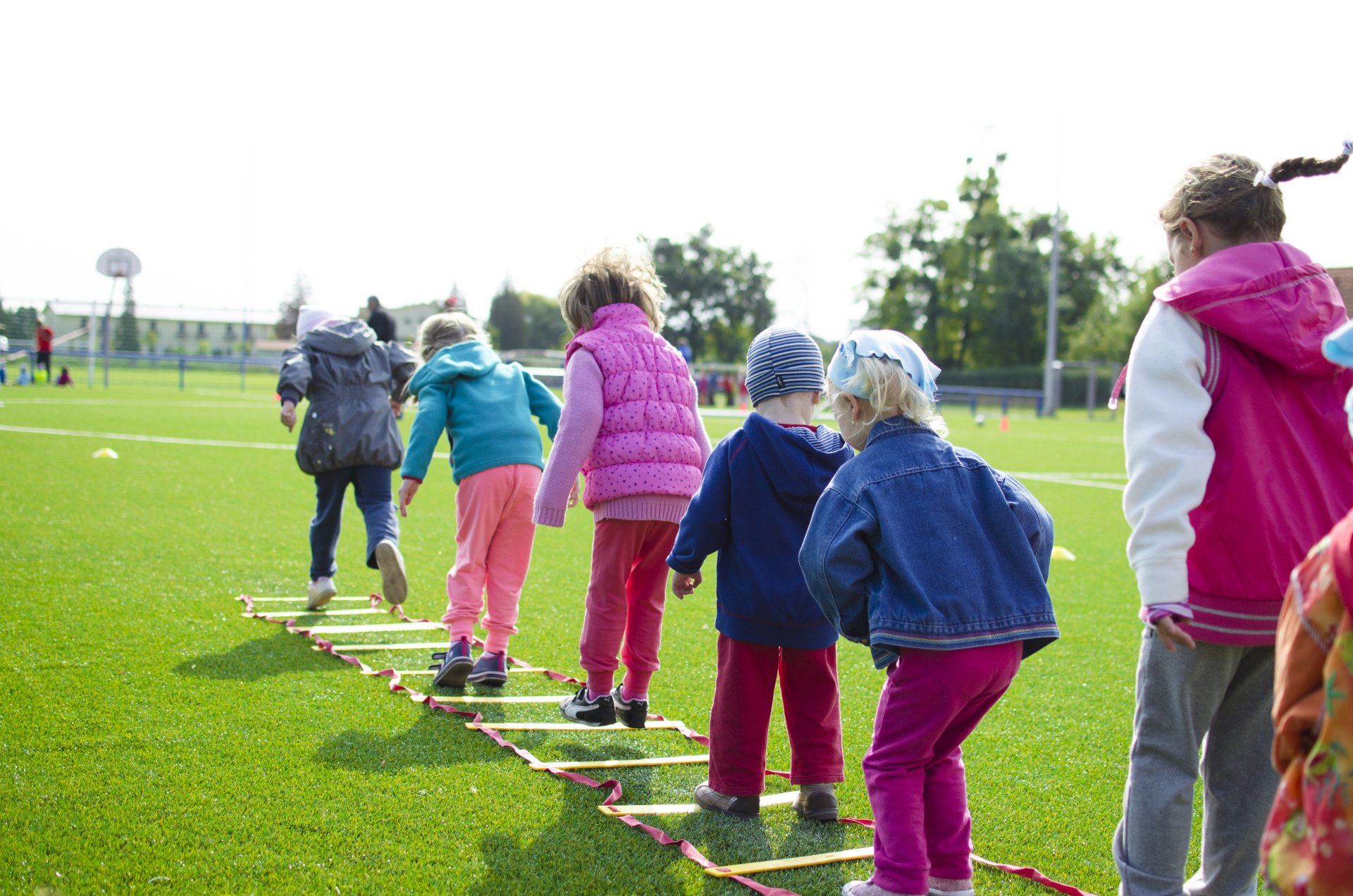 Children standing on a balance rope outdoors during a team activity on a grassy field.
