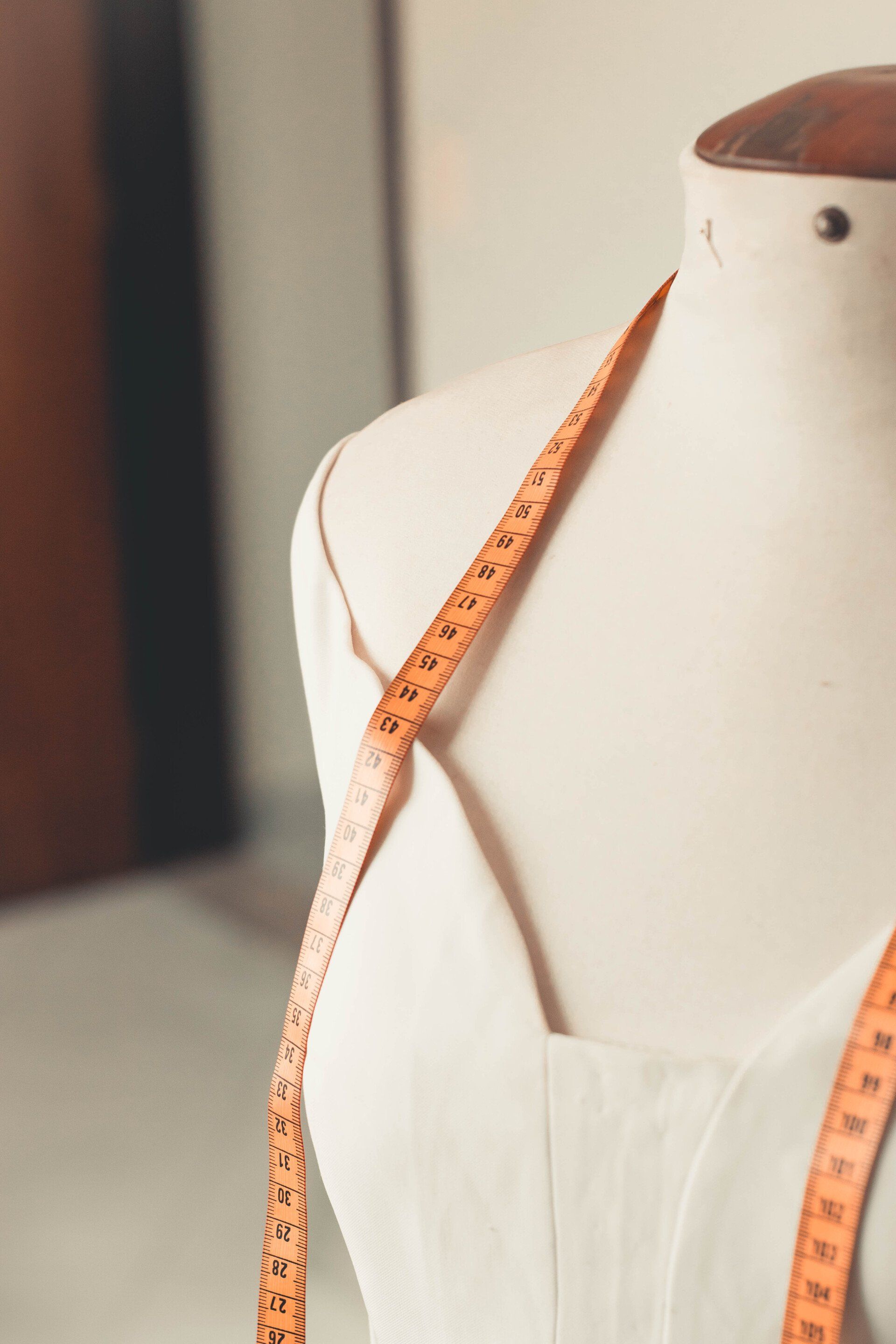 Mannequin with measuring tape draped across the shoulders and a white dress.