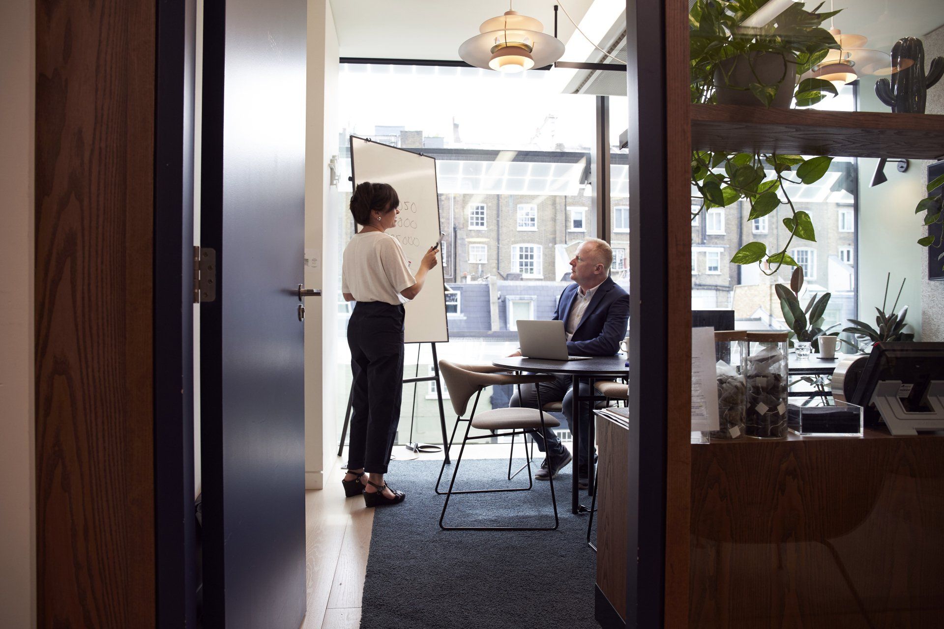 Picture of a woman giving a presentation in a windowed office to a man in a suit
