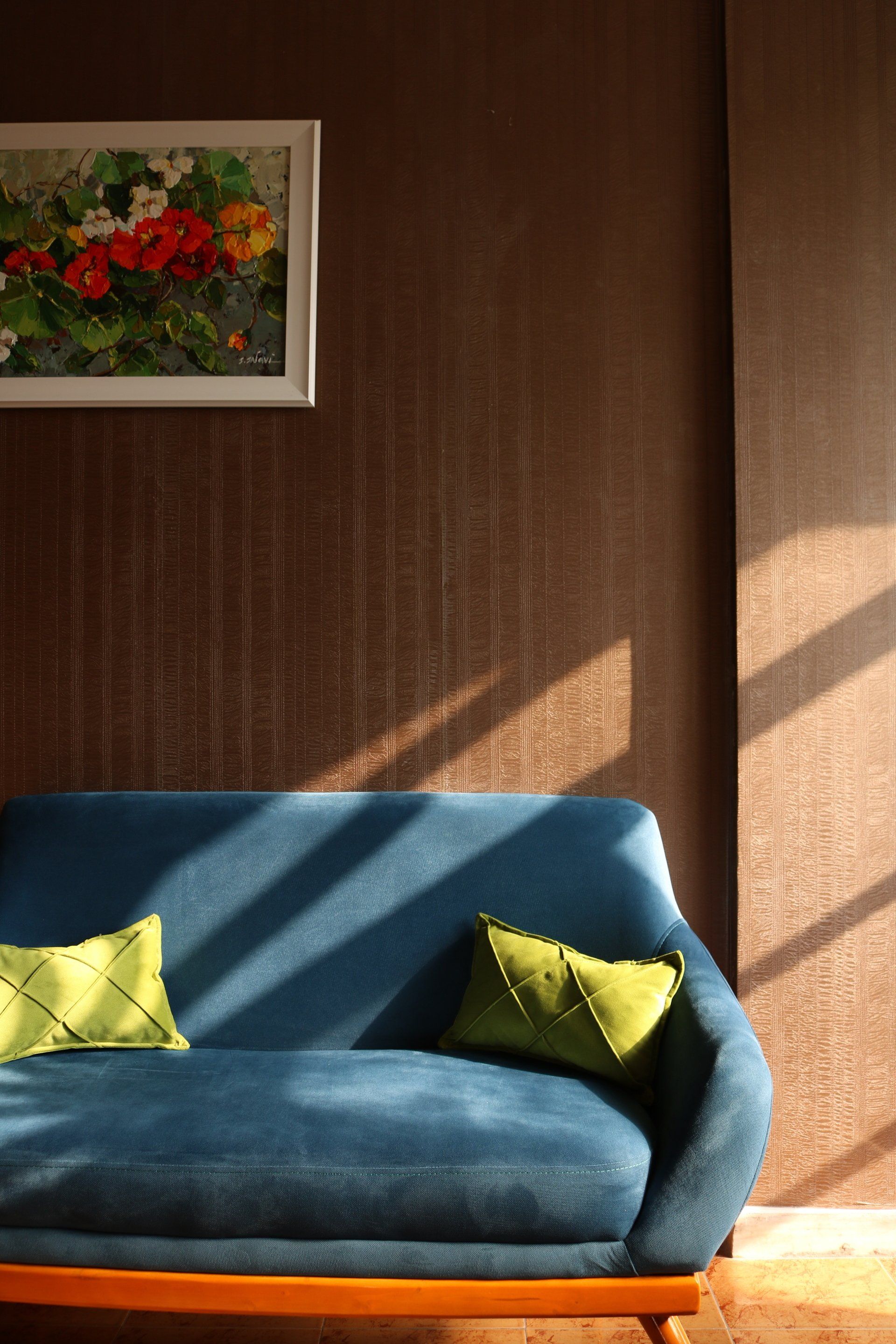 A blue couch with green pillows in front of a brown wall