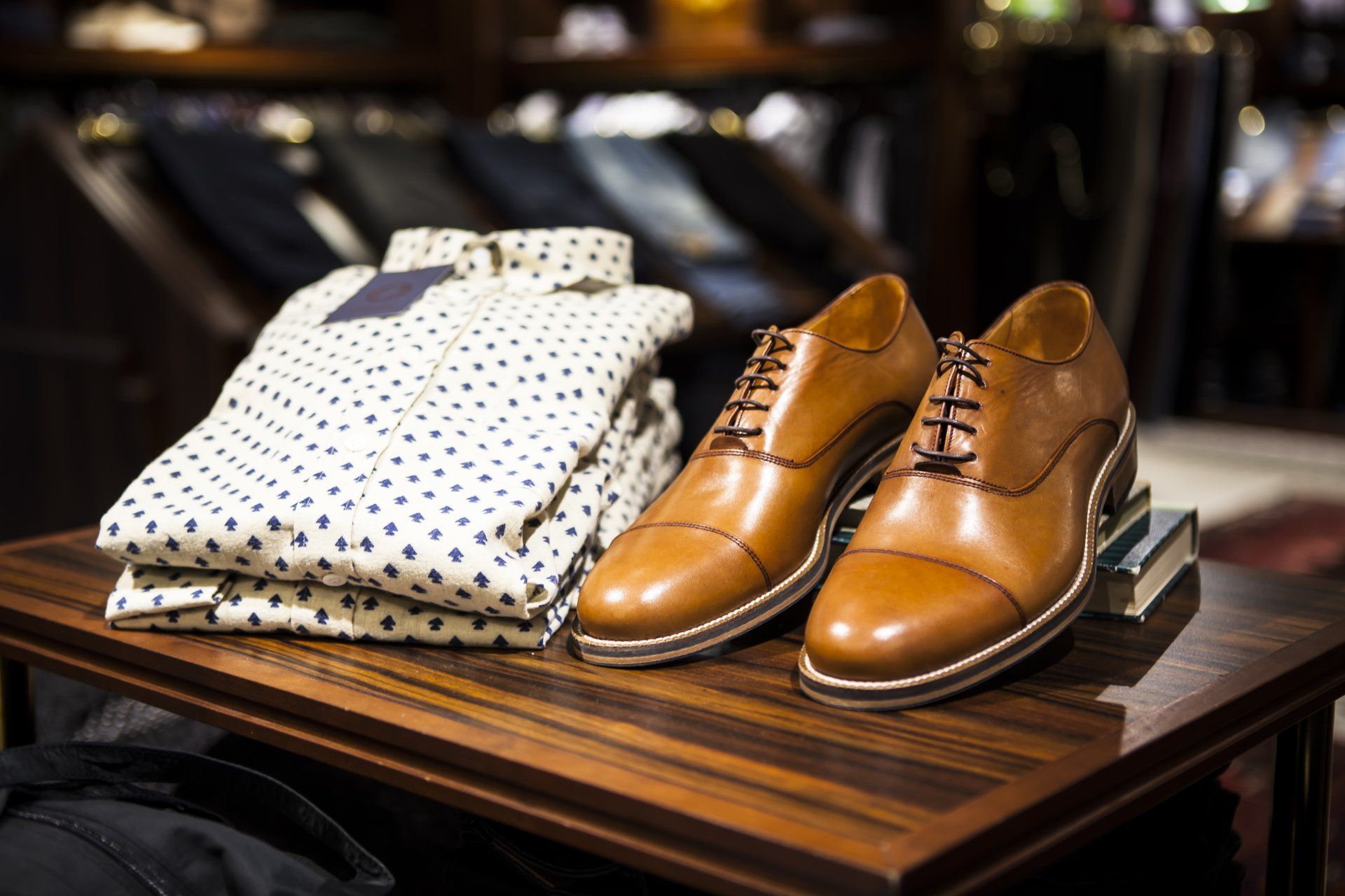 A pair of brown shoes sitting on top of a wooden table next to a stack of shirts.