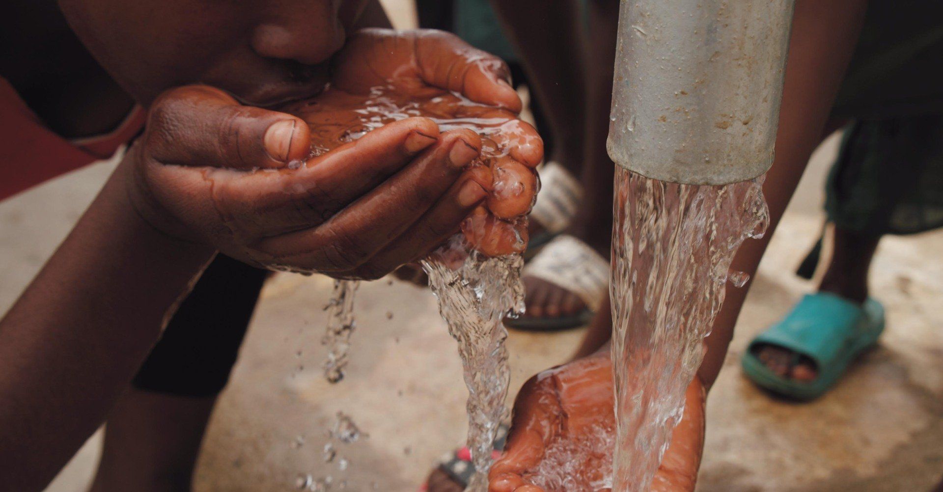 Hands being washed under running water from a tap outdoors.