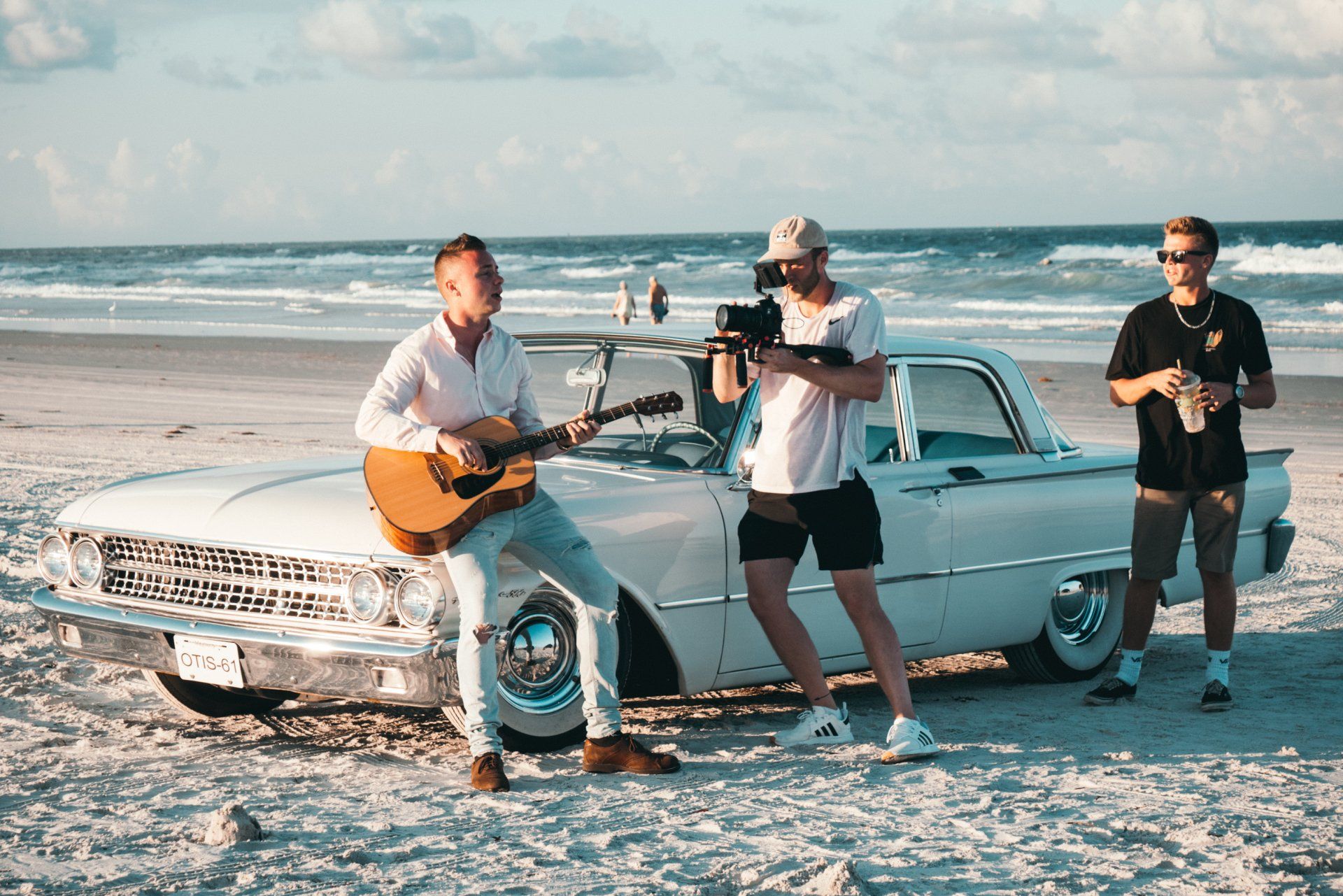 Três homens estão parados ao lado de um carro branco na praia.