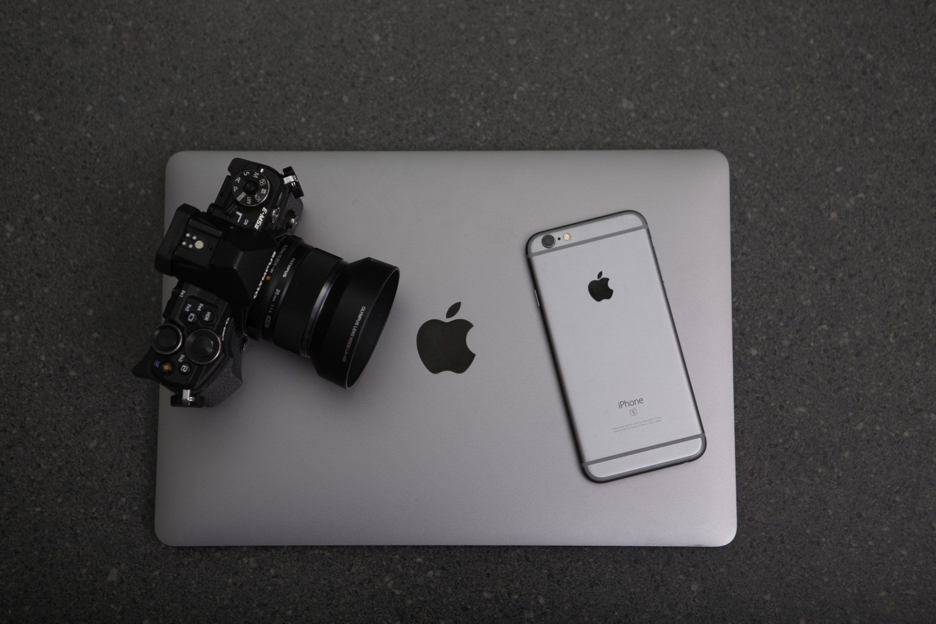 Black camera on a silver MacBook with an iPhone outline, viewed from above.