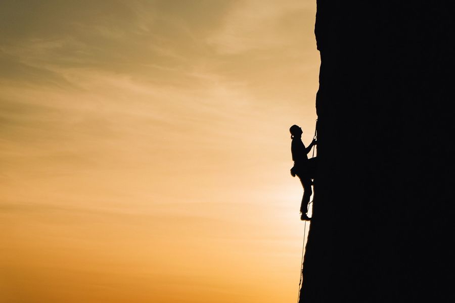Die Silhouette einer Person, die bei Sonnenuntergang eine Felswand erklimmt.