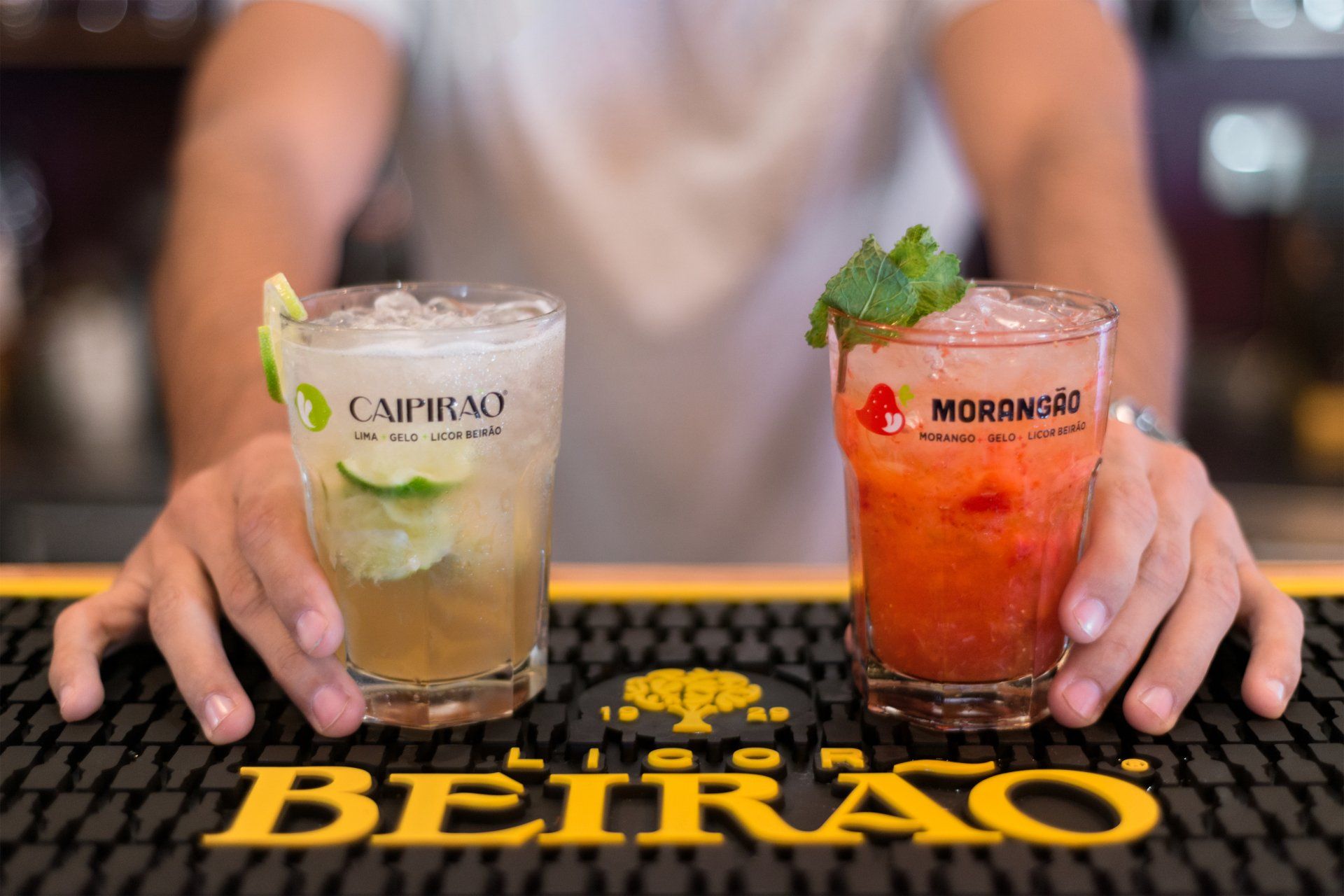 Bartender holding two cocktails on a bar; one lime, one strawberry.