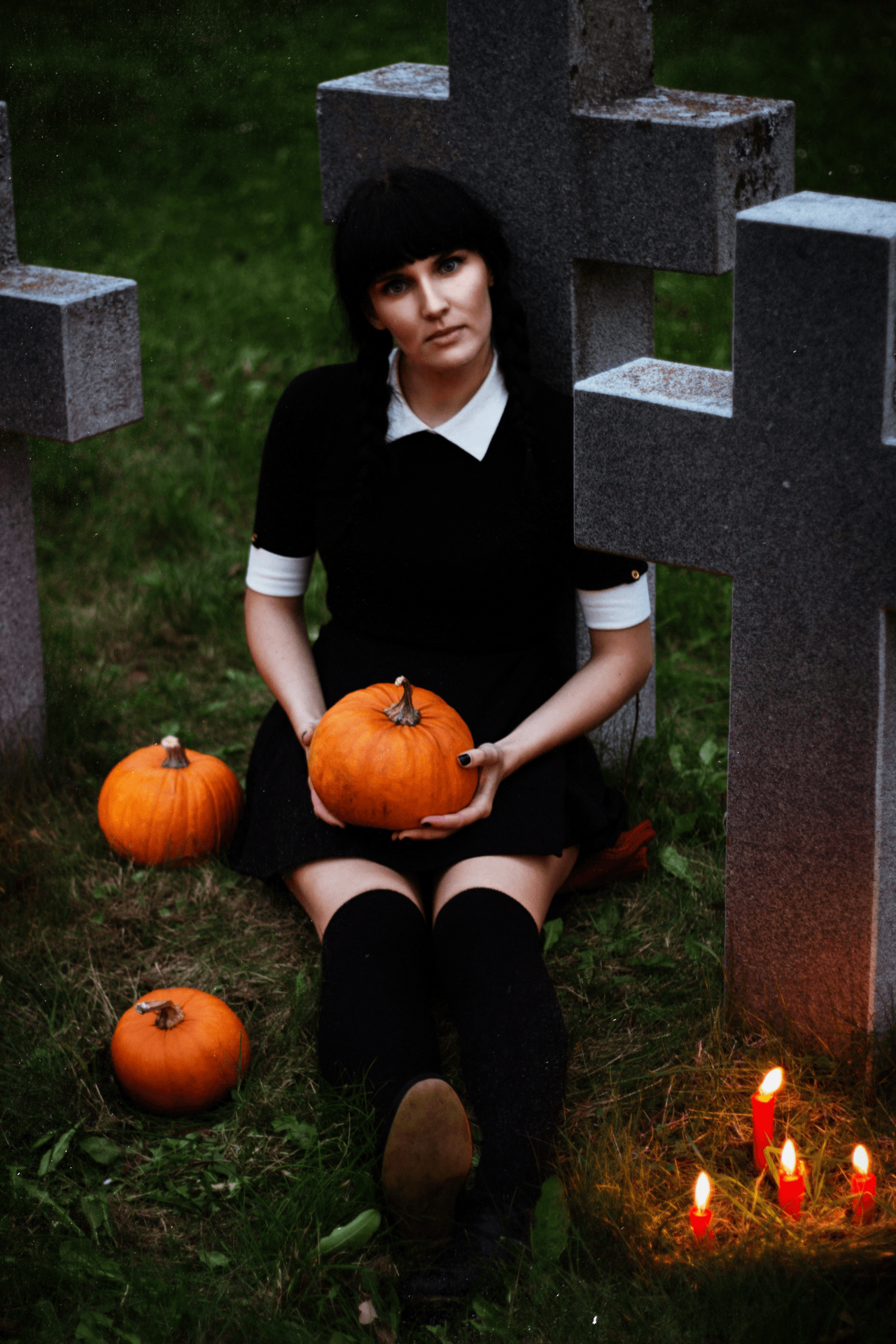 a woman in a black dress is sitting in a cemetery holding a pumpkin .
