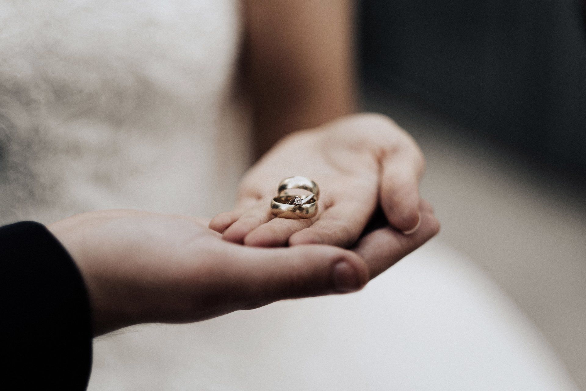 A bride and groom are holding their wedding rings in their hands.