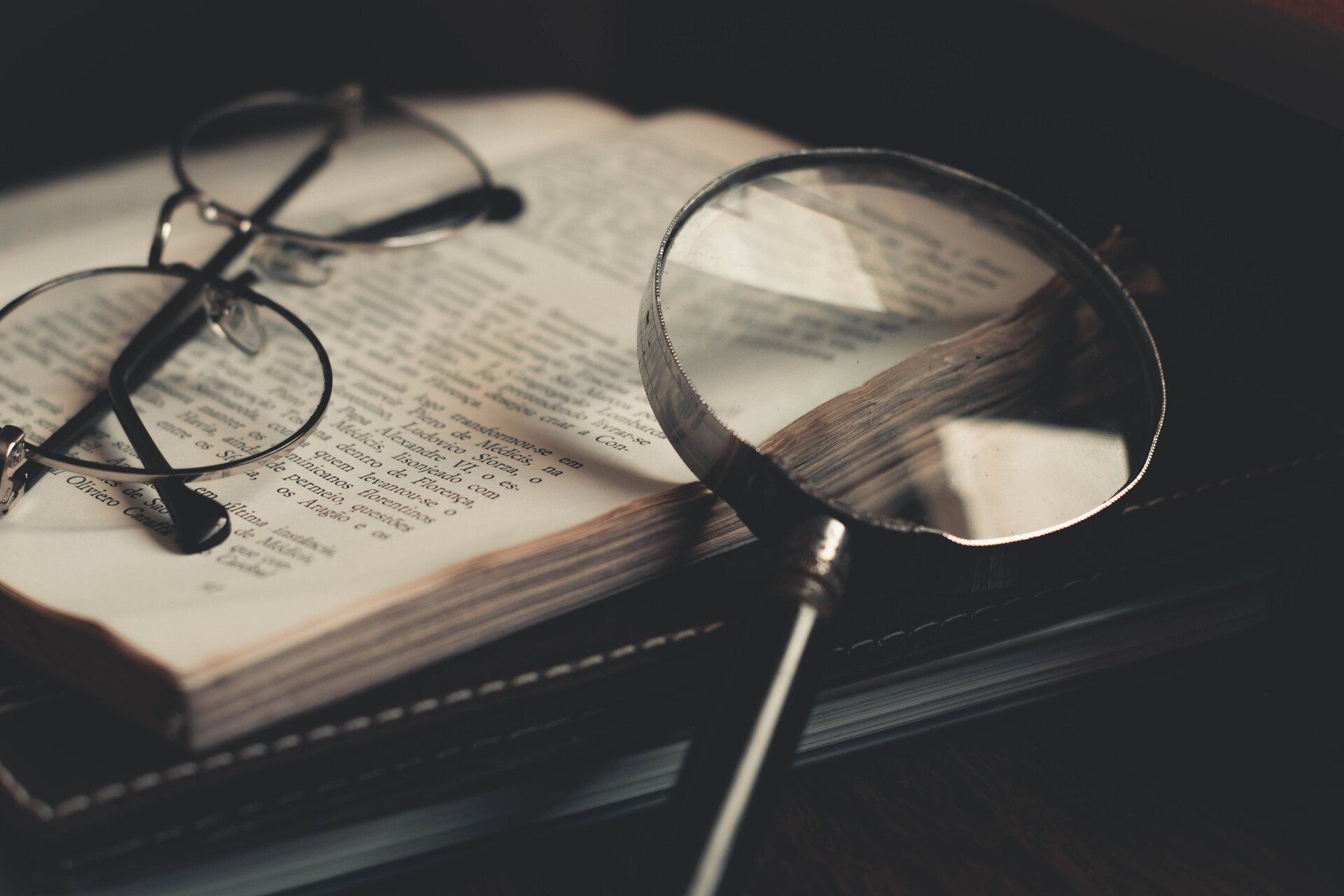 Open book with eyeglasses and magnifying glass on top.