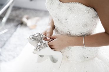 La sposa tiene in mano un bouquet bianco tempestato di gioielli, indossa un abito da sposa senza spalline e un braccialetto.