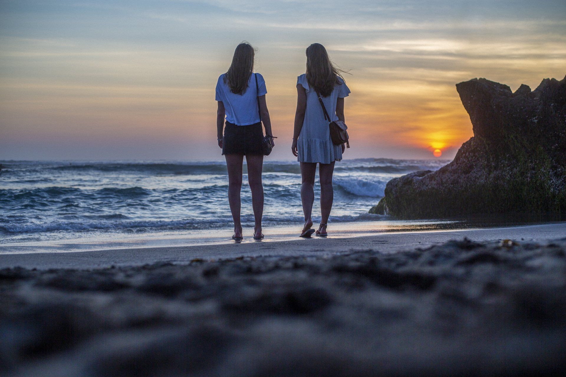 Two women are standing on a beach at sunset.