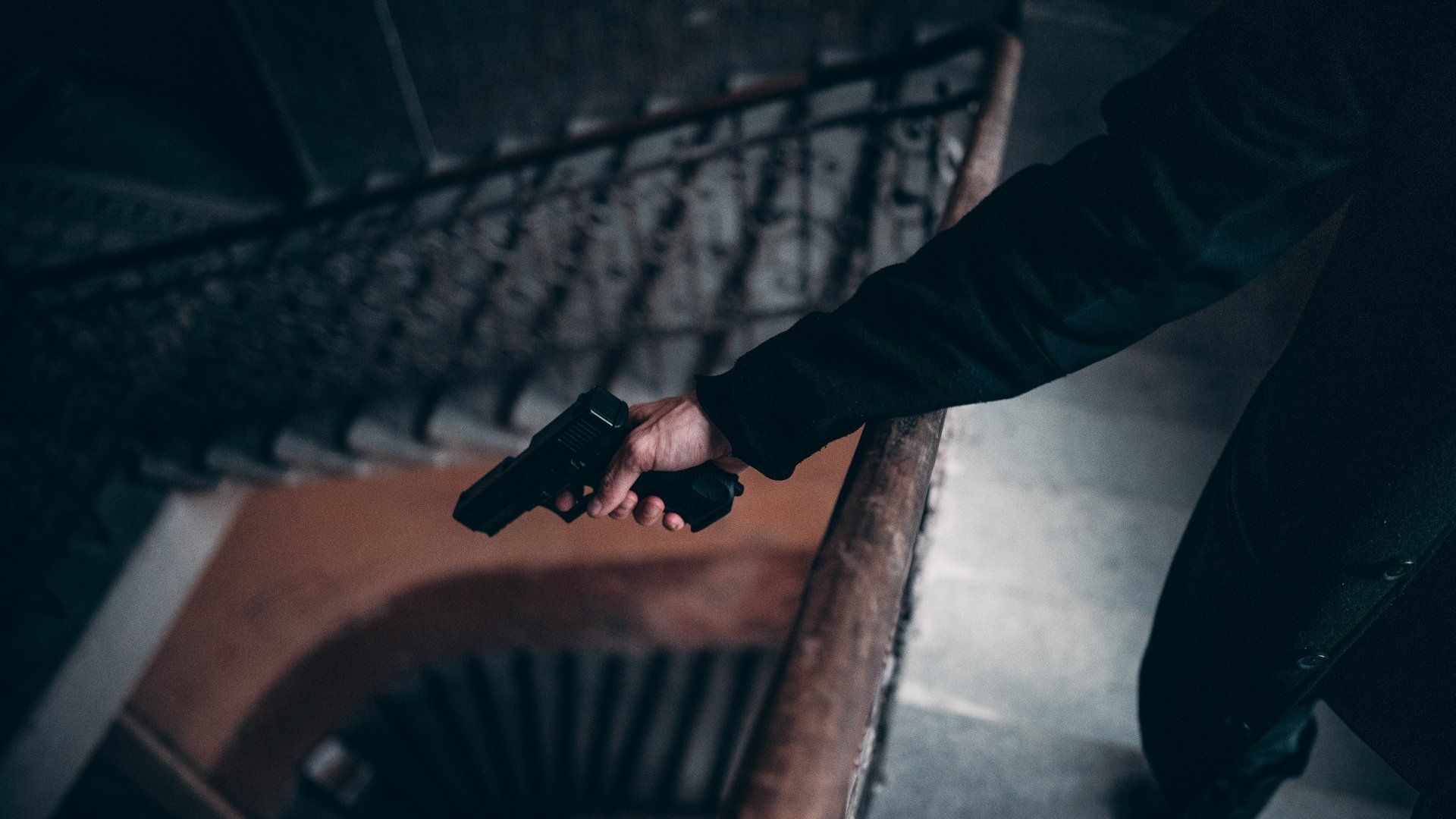 Person holding a handgun in a stairwell, pointing it downwards.