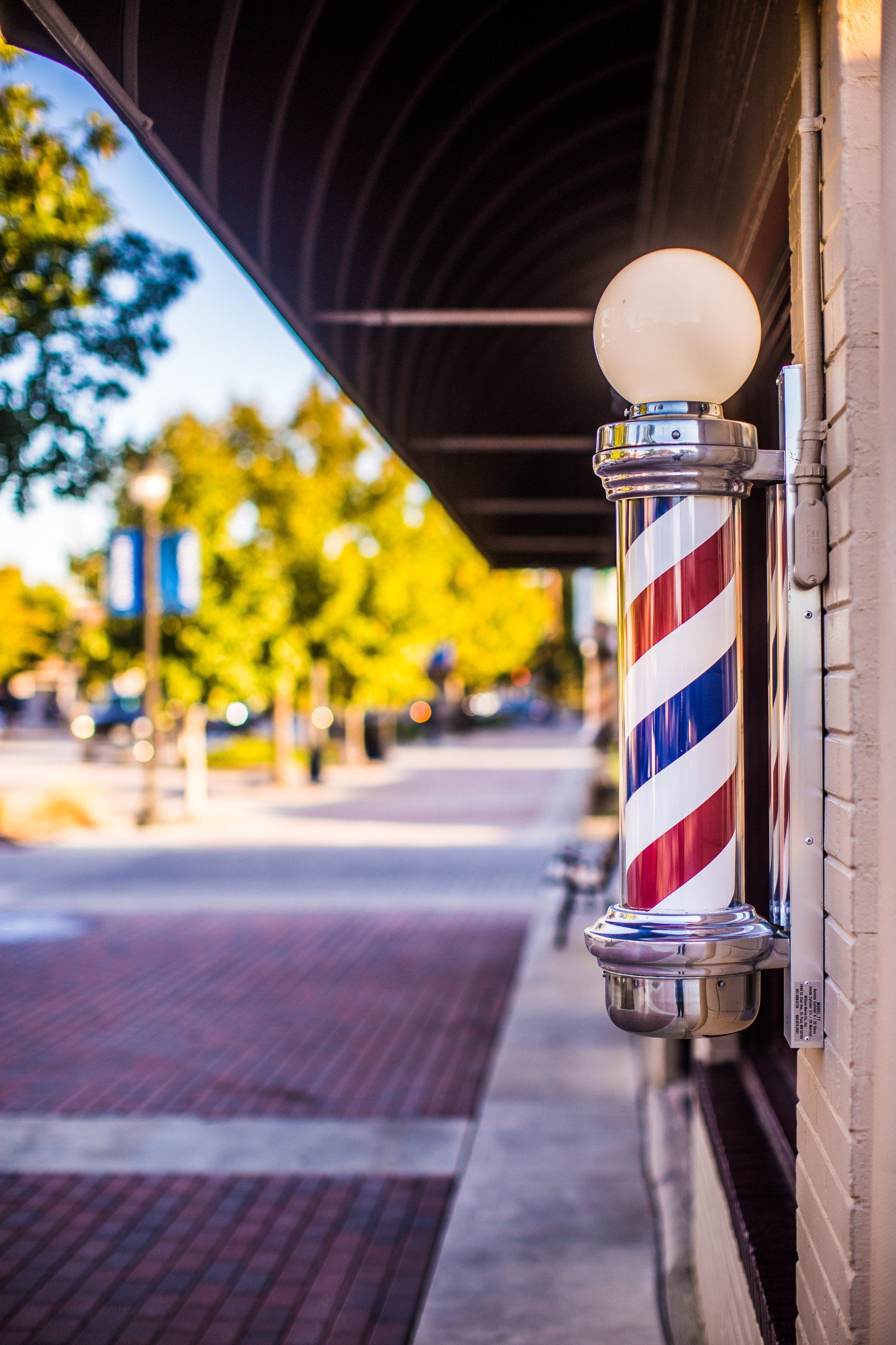 Barber pole with red, white, and blue stripes outside a brick building on a city street.