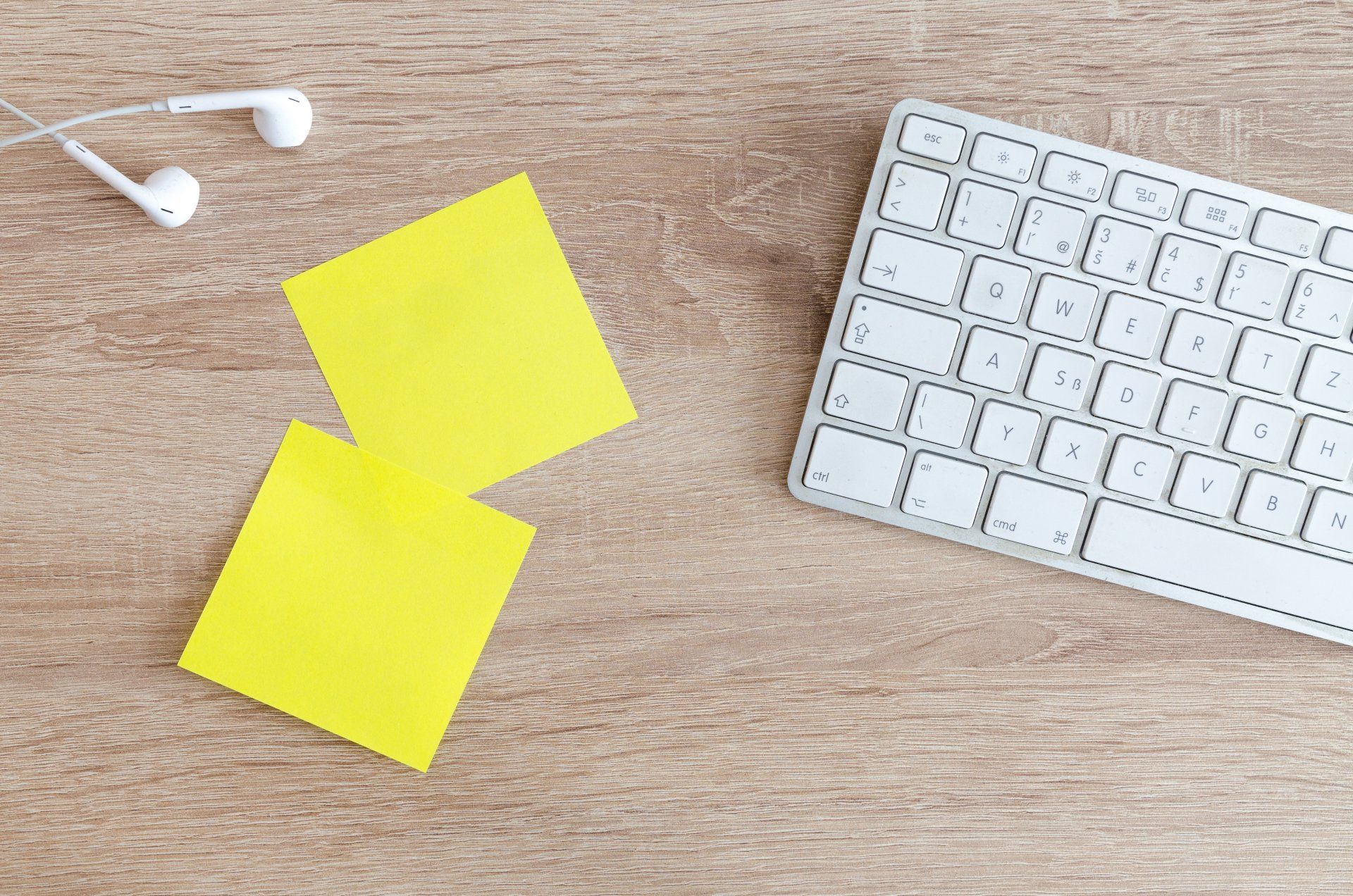 Um teclado, fones de ouvido e dois post-its amarelos sobre uma mesa de madeira.