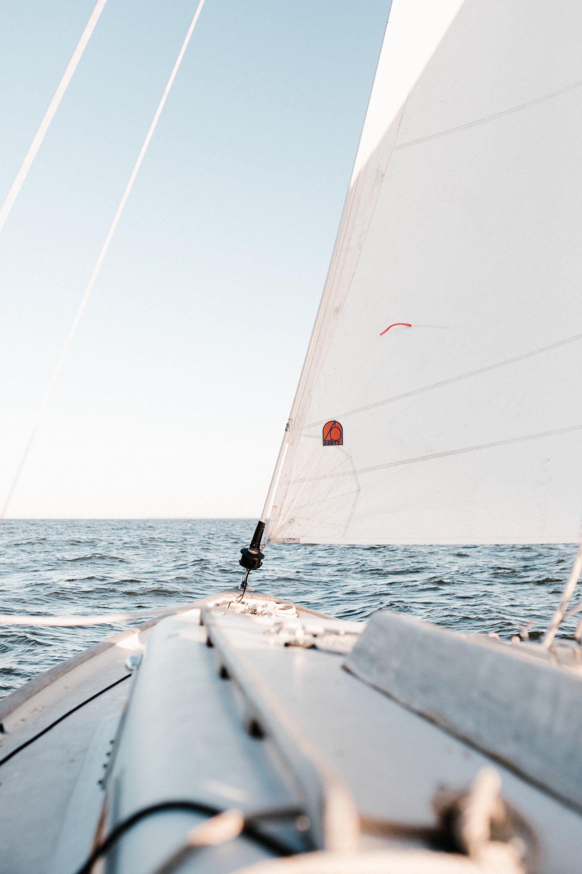 Velero sobre el agua con velas blancas, flotando al viento. Cielo azul.