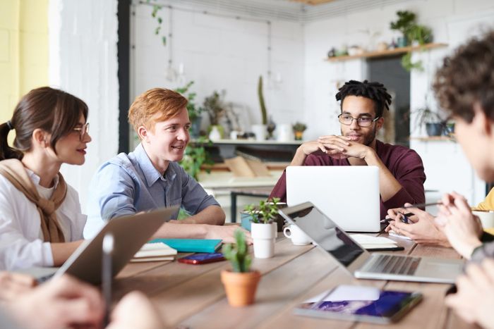 A group of people are sitting around a table with laptops.