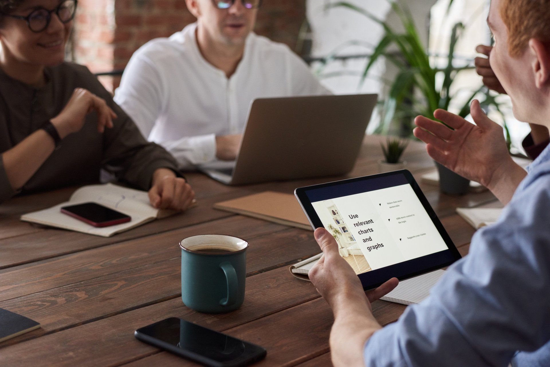 A group of people are sitting around a table with laptops and a tablet.