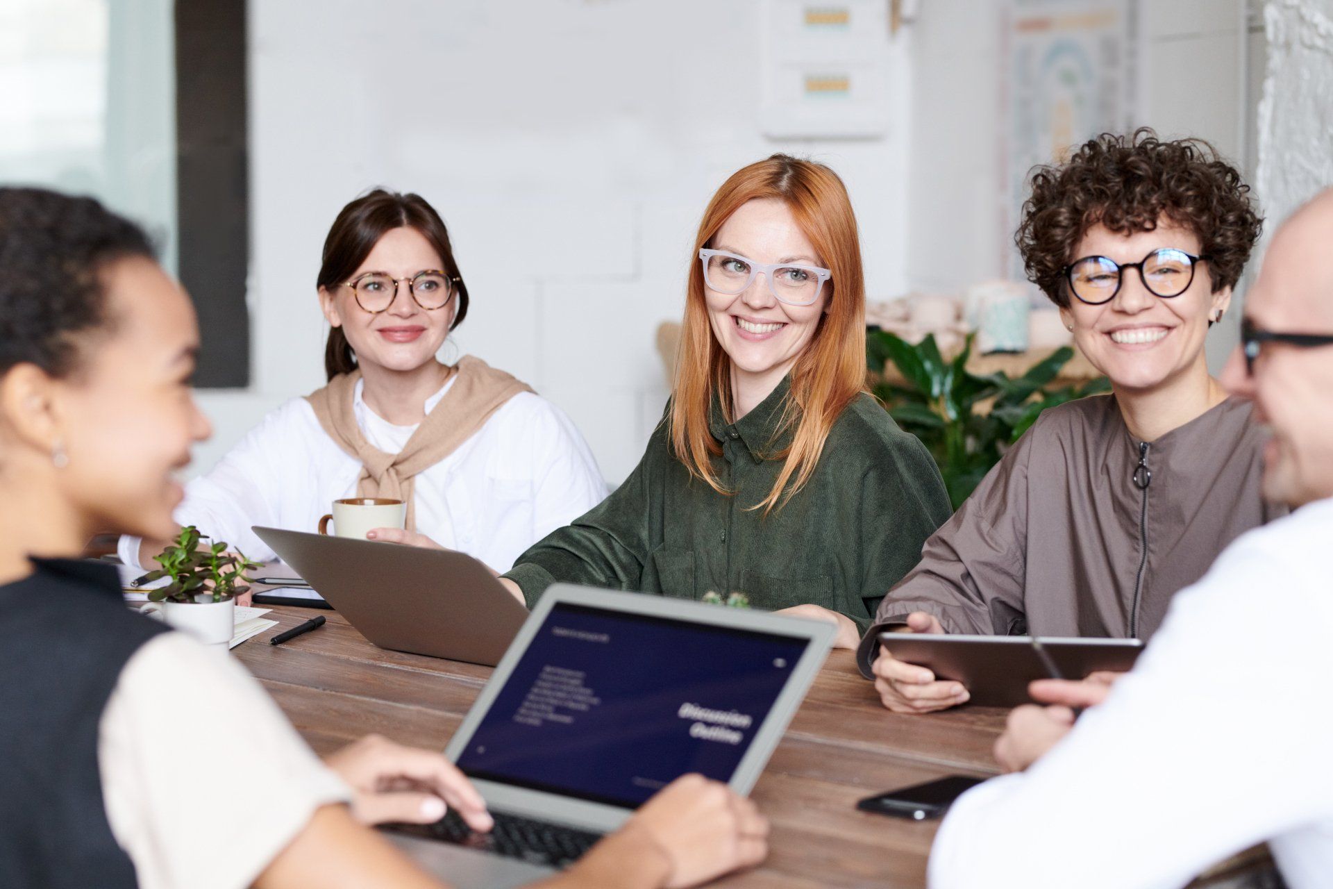A group of people are sitting around a table with laptops and tablets.