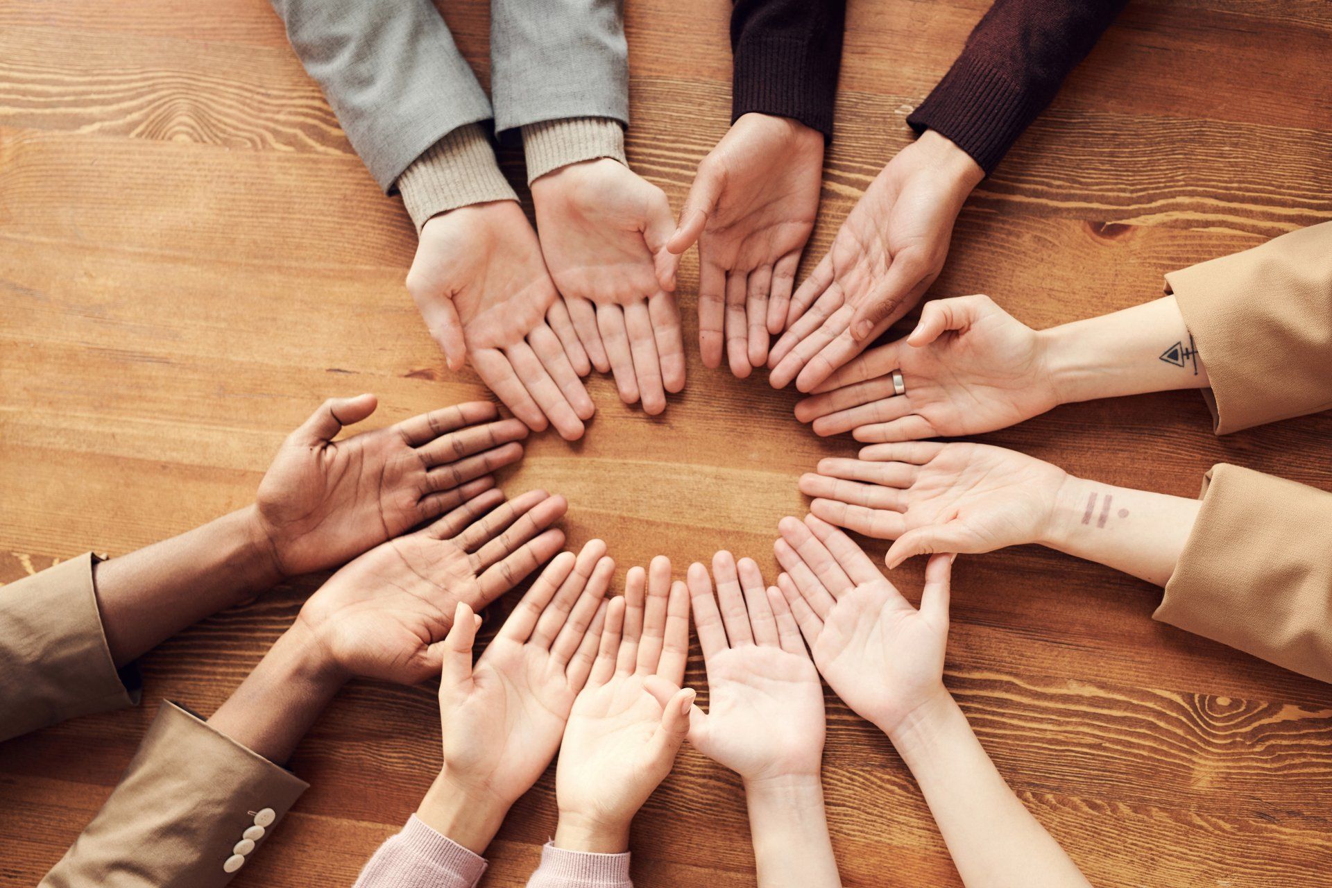 A group of people are putting their hands together in a circle on a wooden table.