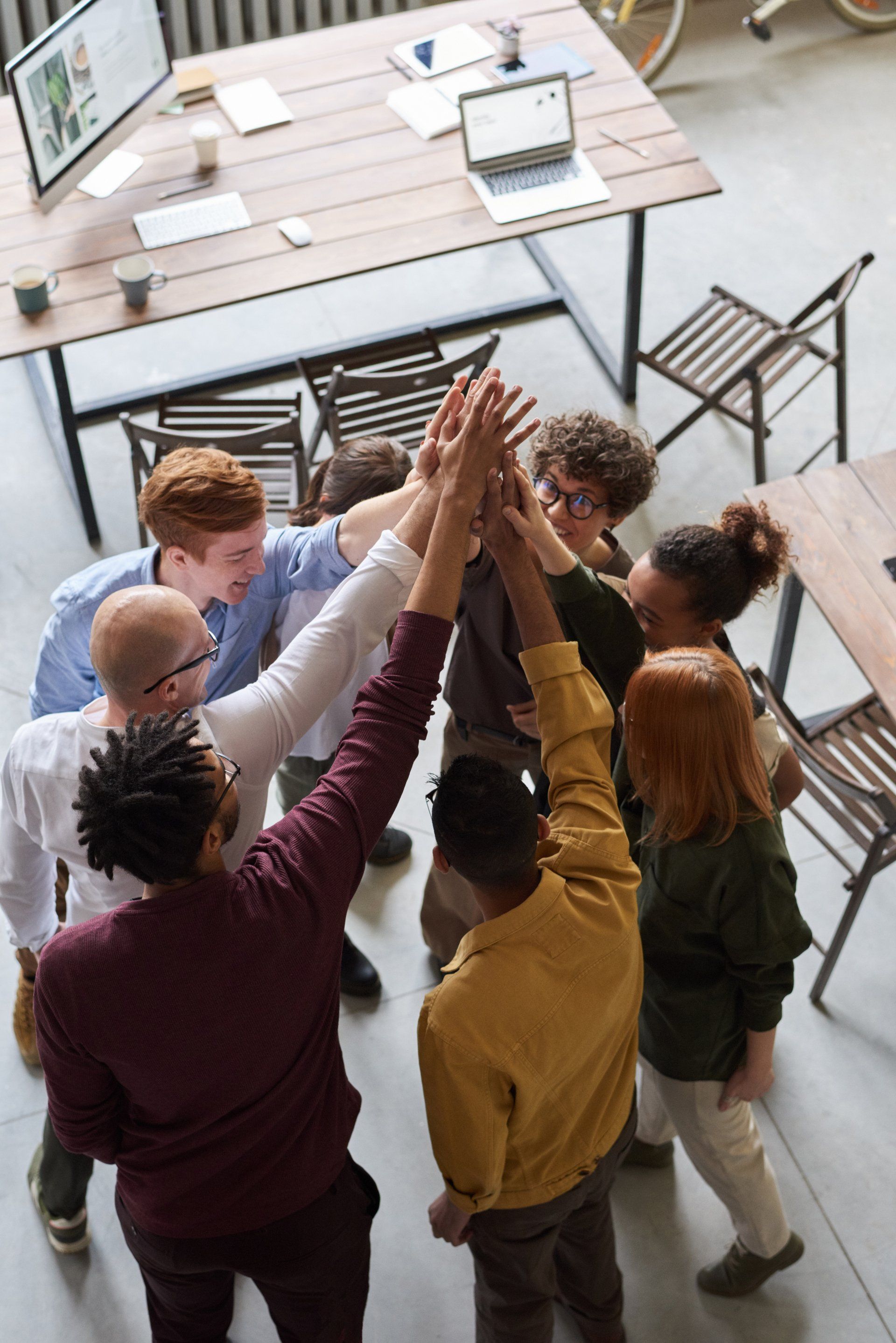 Group of coworkers high-fiving in an office meeting area, viewed from above, around a wooden table