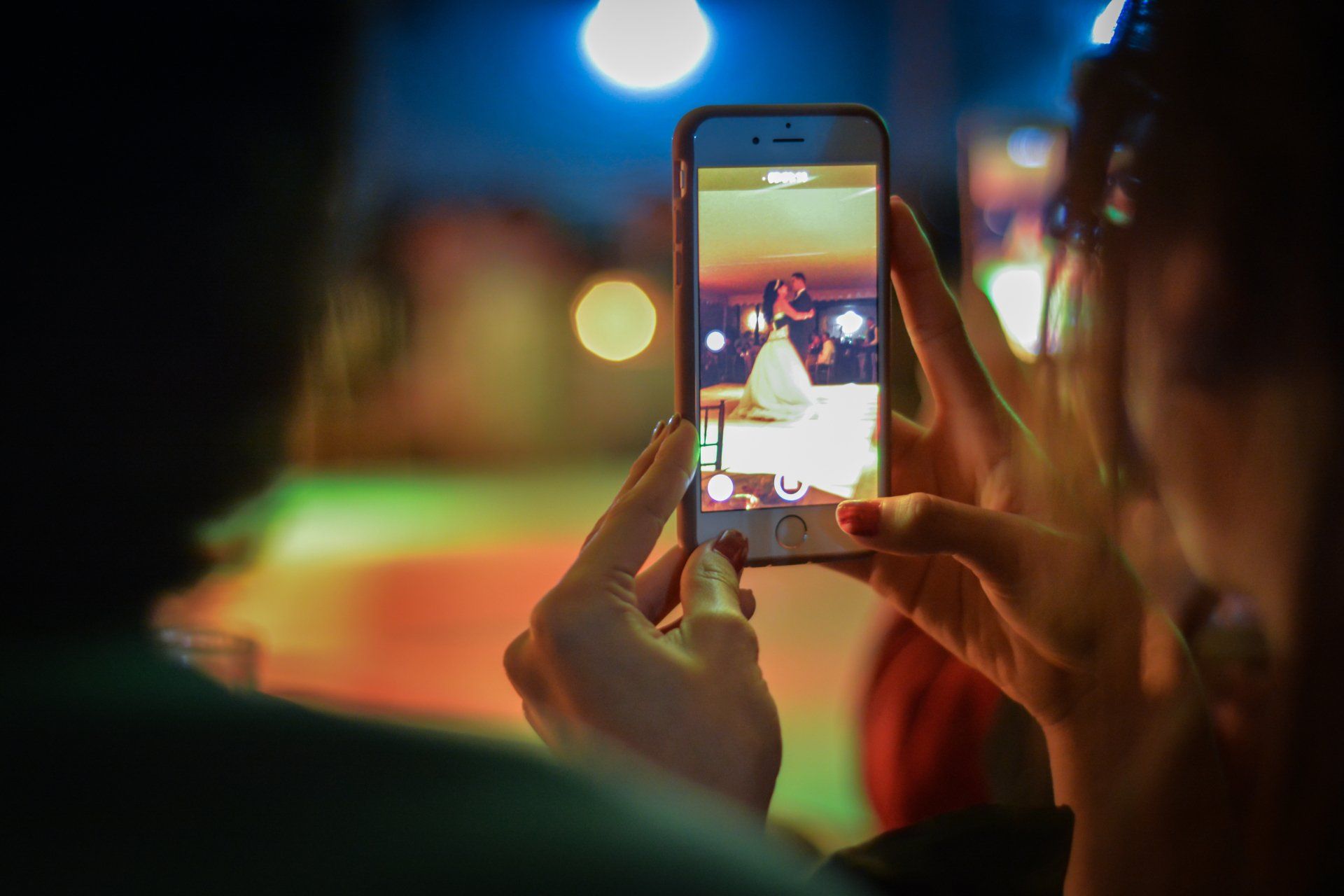 A woman is taking a picture of a bride and groom on a cell phone.