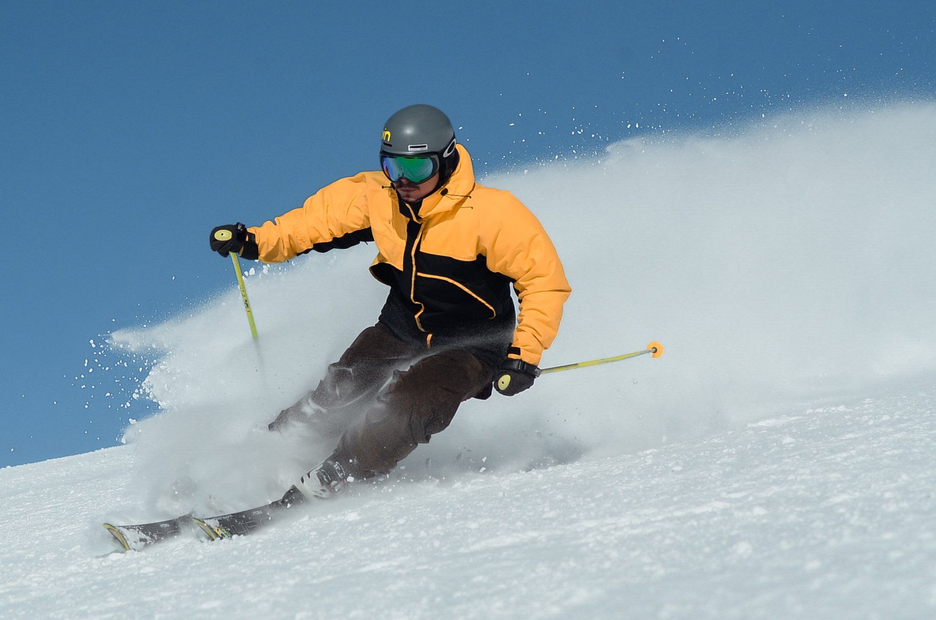 En mann i gul jakke går på ski ned en snødekt skråning
