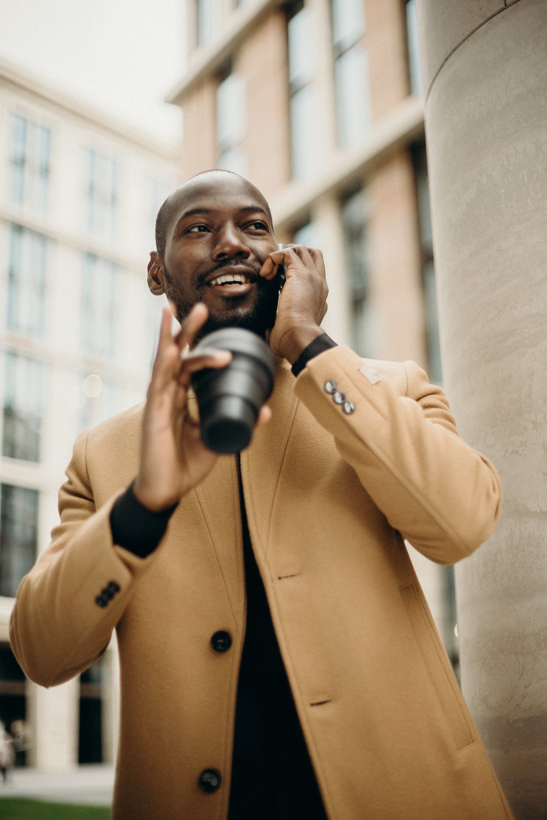 A man in a beige jacket is holding a camera and talking on his cell phone.