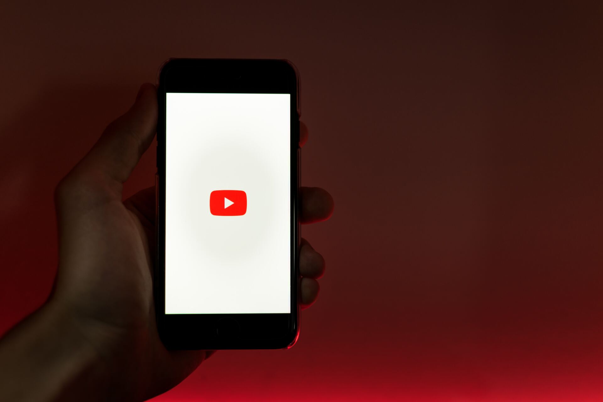 A person is holding a cell phone with a youtube logo on the screen.