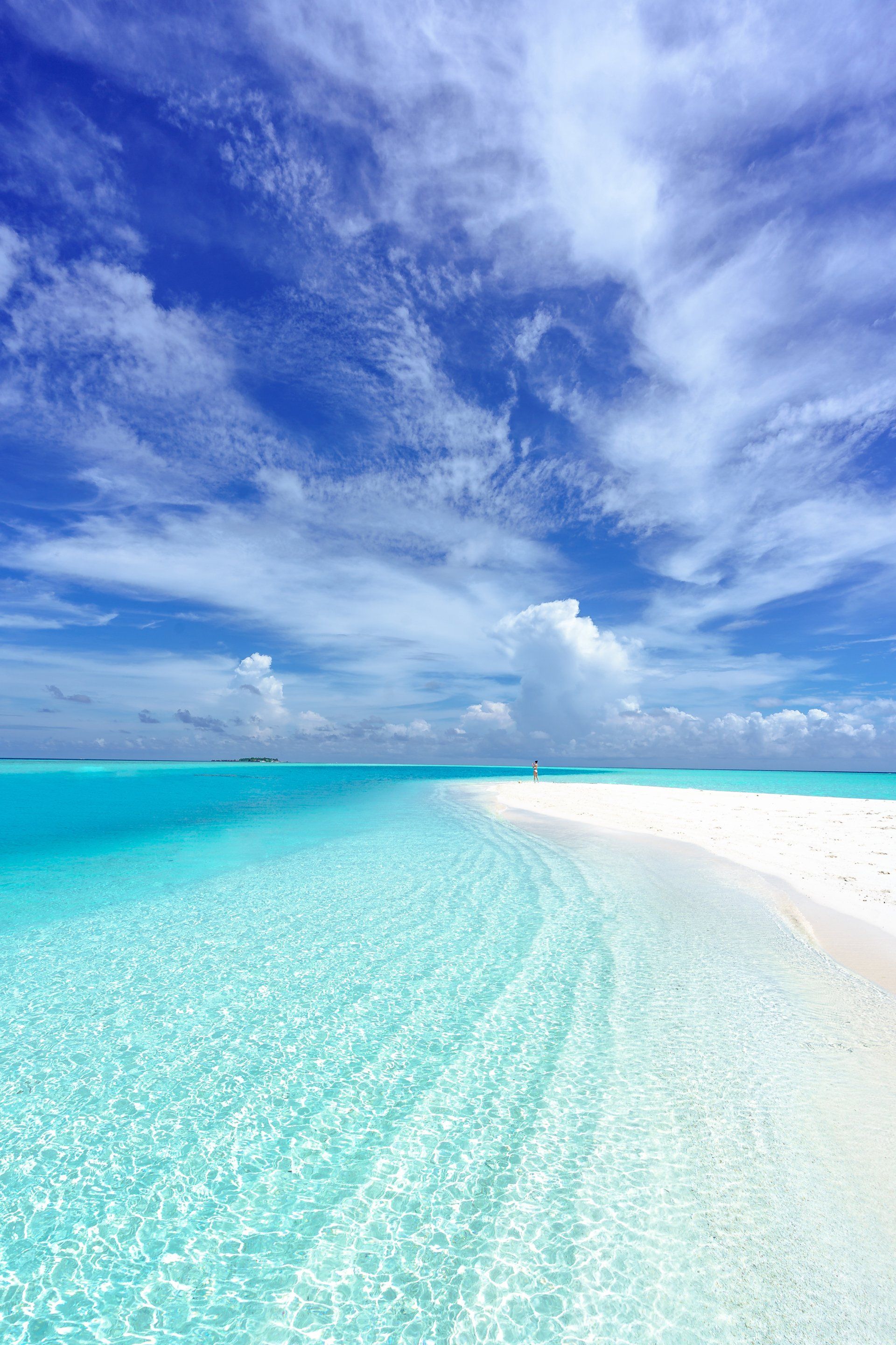 Weißer Sandstrand mit kristallklarem, türkisfarbenem Wasser unter blauem Himmel mit flauschigen Wolken.
